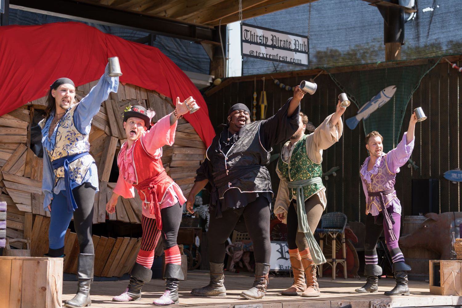 Performers in colorful costumes dance energetically on an outdoor stage during a festival performance.