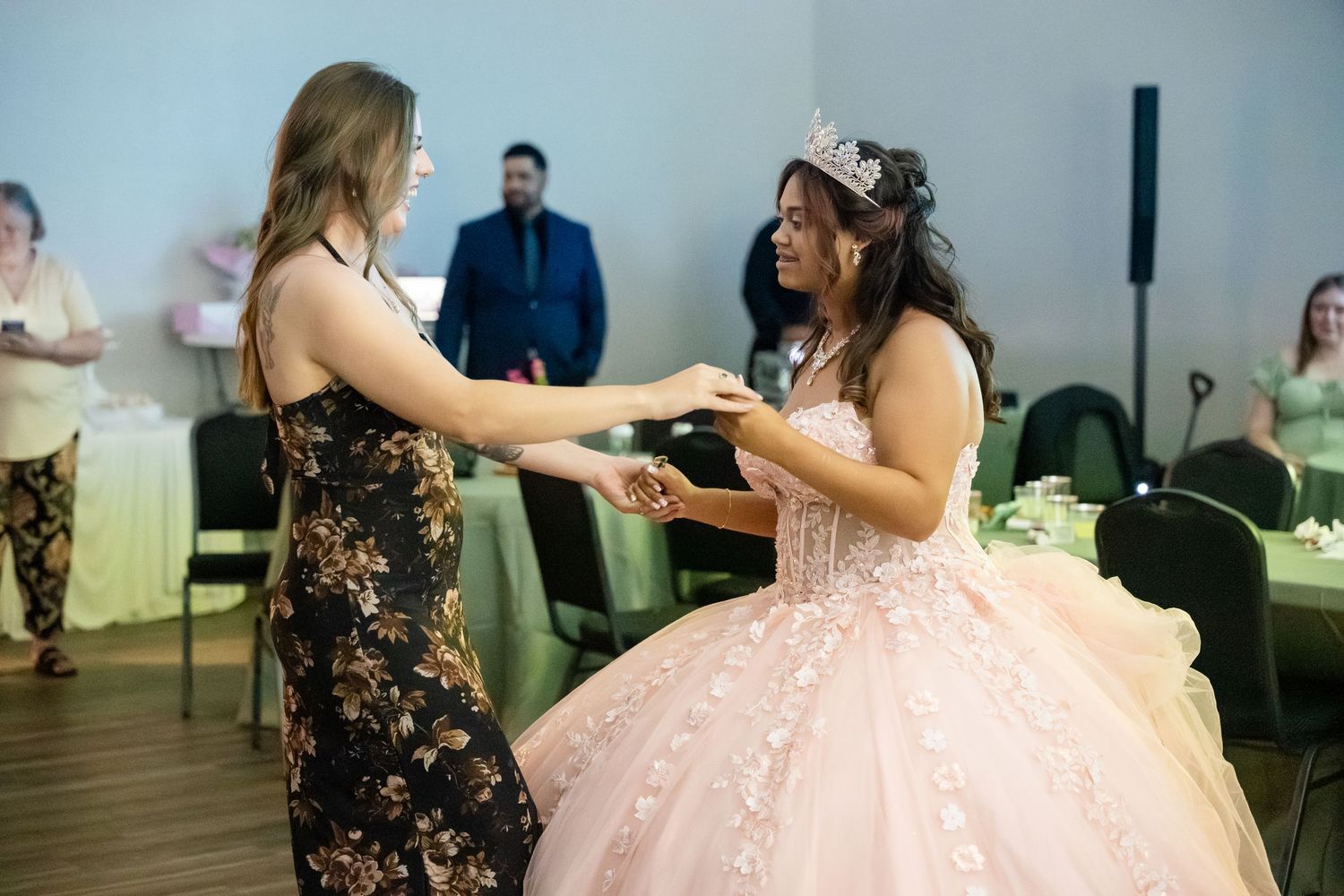 Two young women dancing together at a quinceañera celebration, one wearing a pink ball gown and tiara.