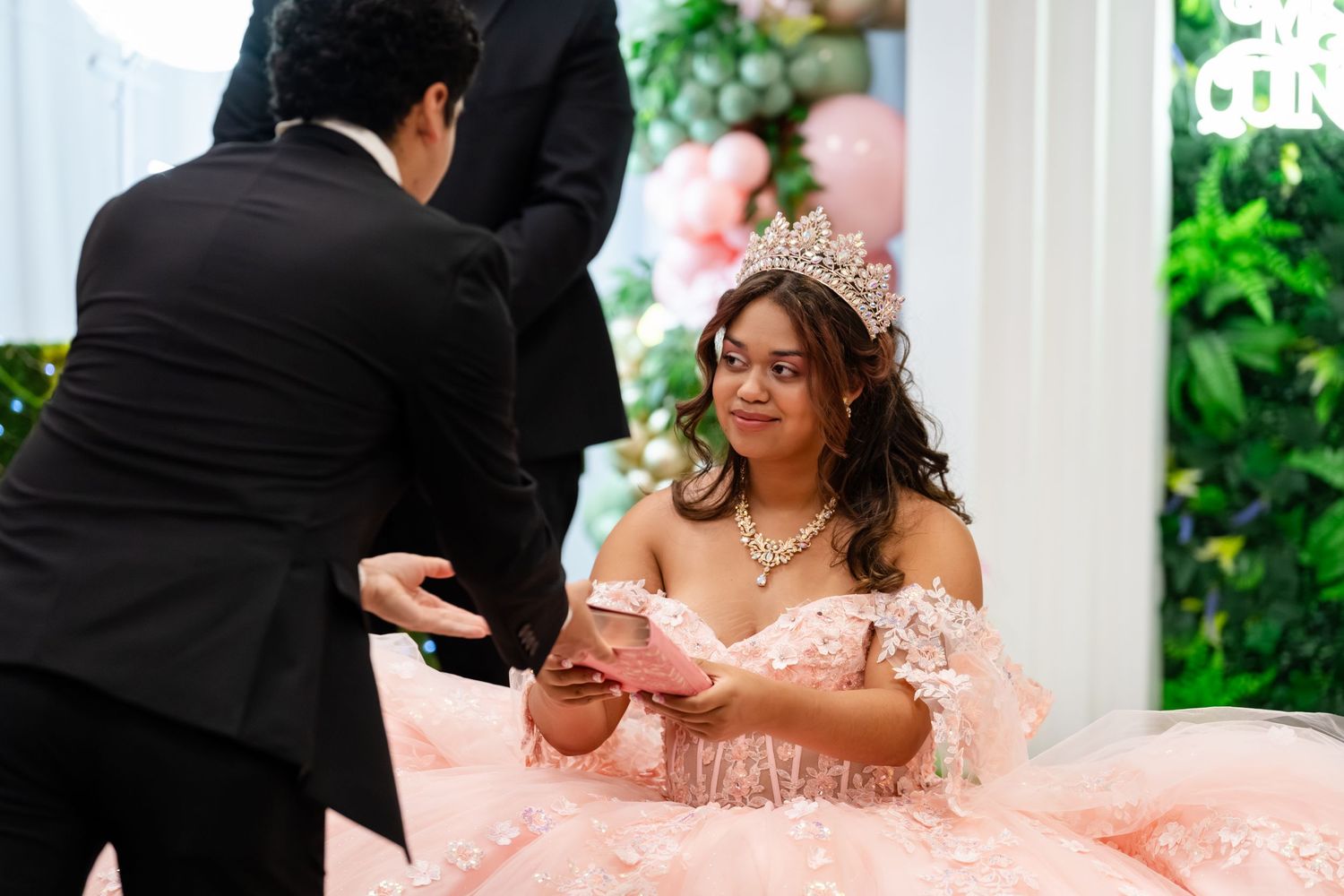 Young woman in pink quinceañera gown and tiara receives a gift during her elegant celebration.