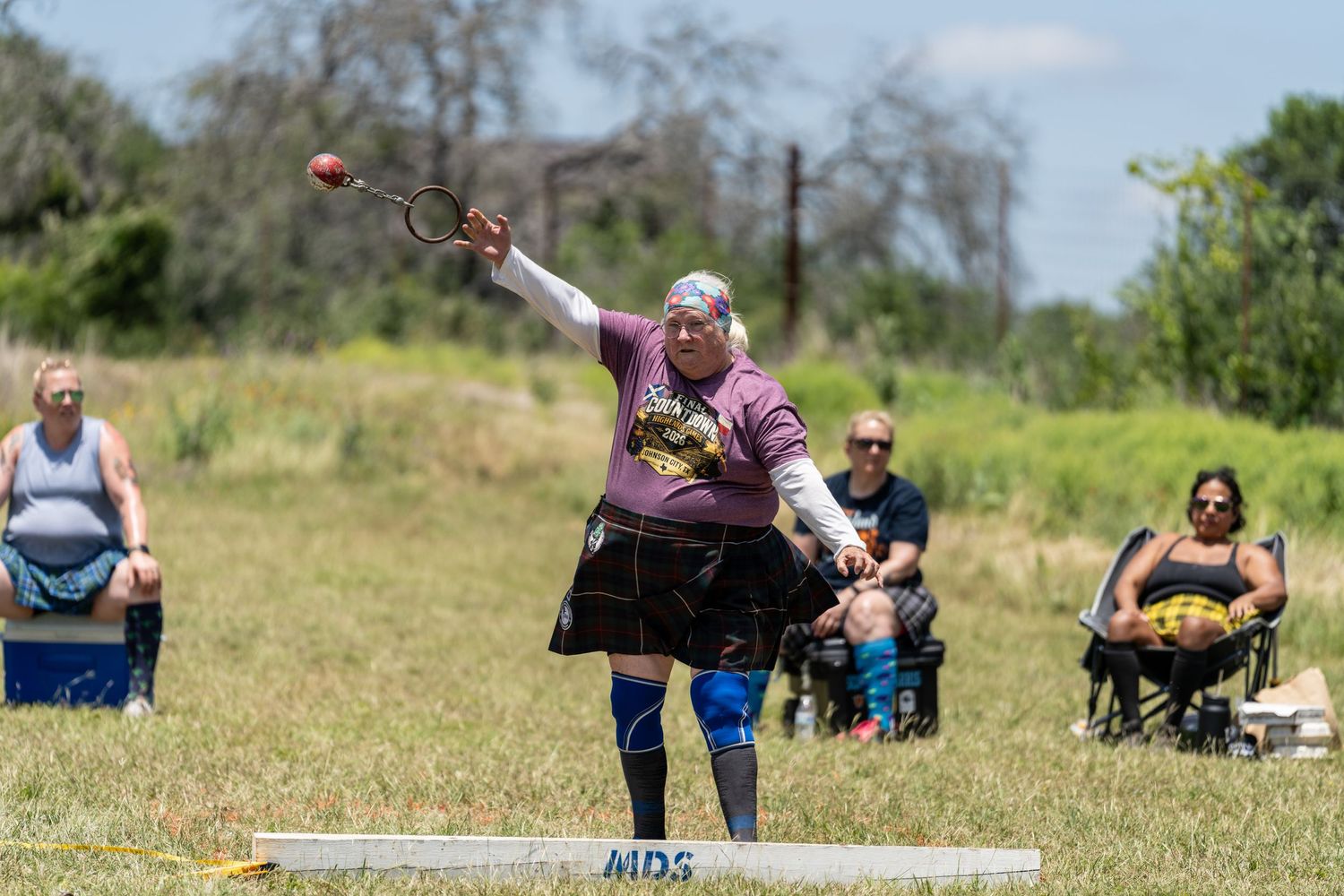 Athlete in kilt competes in Highland Games hammer throw event outdoors, spectators watching in background.