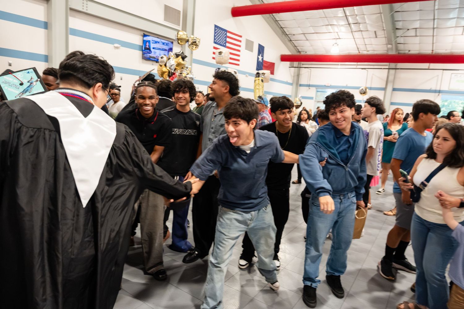 Students celebrate with a graduate in cap and gown at an indoor graduation ceremony.