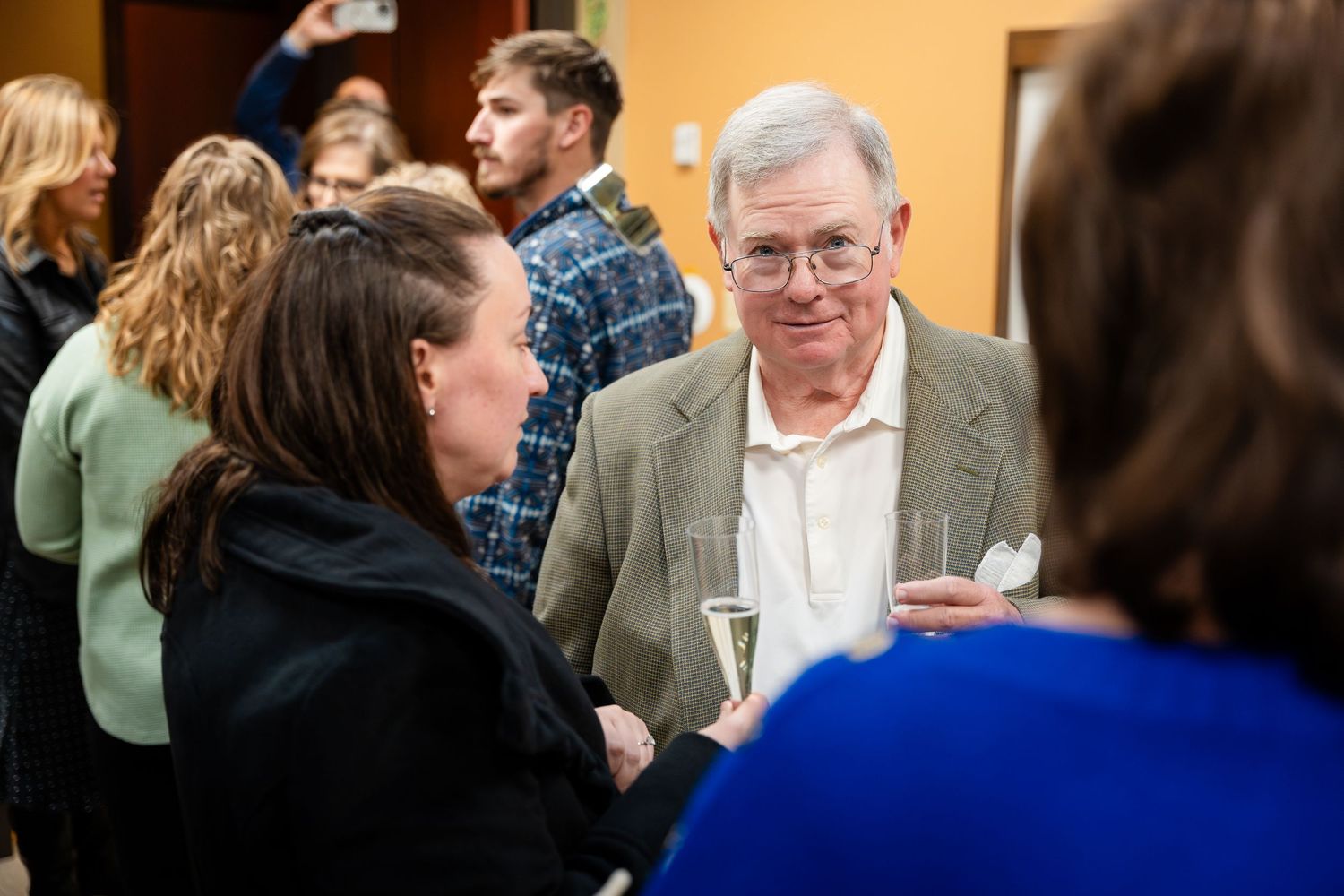 People engaged in conversation at a casual networking event with an orange wall backdrop and blurred figures in the background.