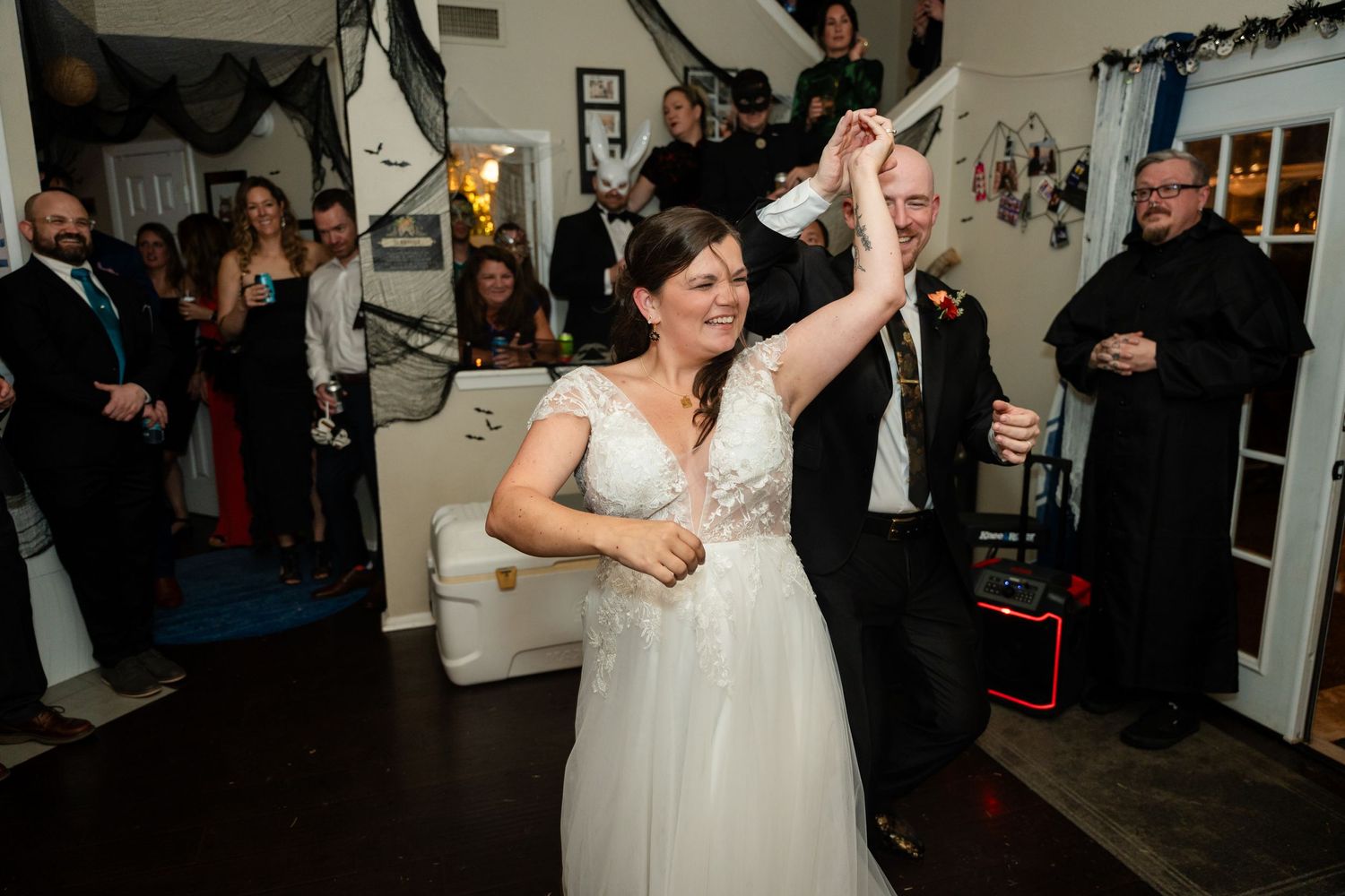 A bride in a white gown dances joyfully at a wedding reception with guests looking on from the background.