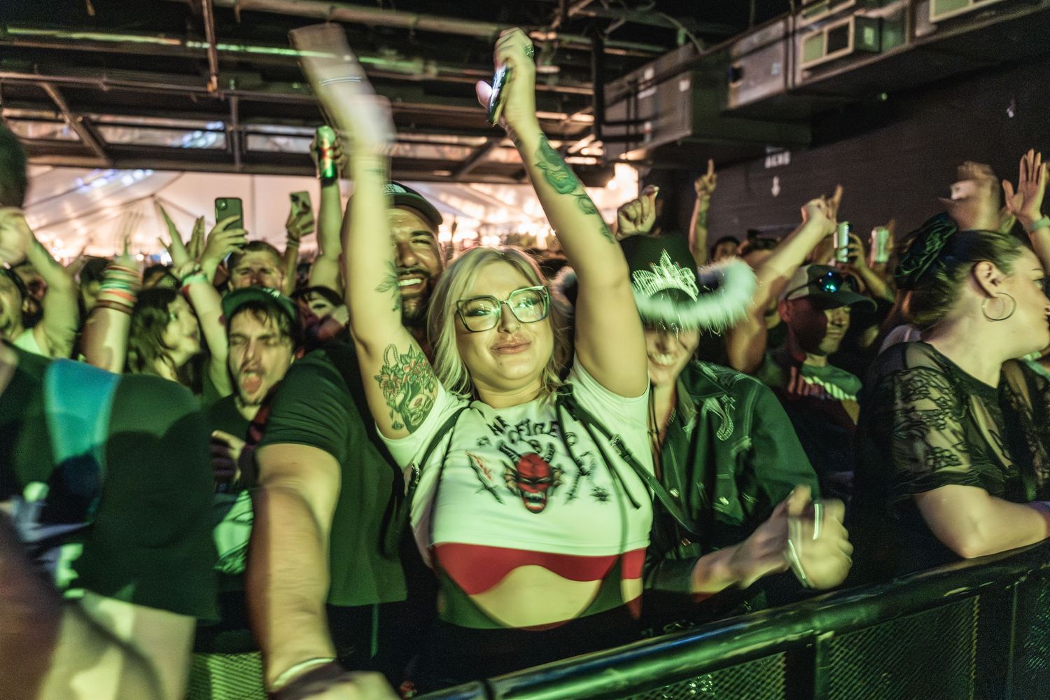 Enthusiastic concert crowd dancing and cheering under green venue lighting.