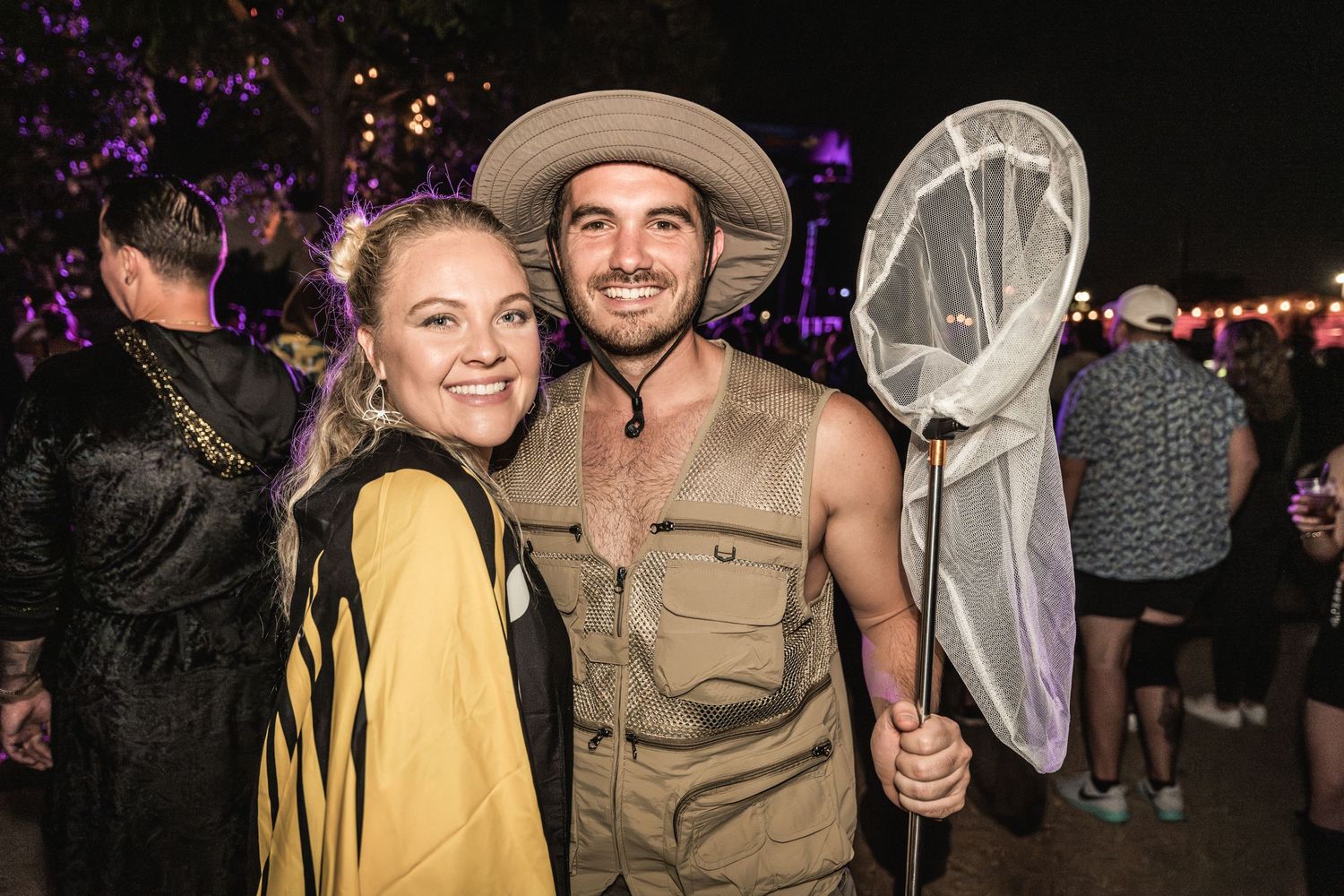 Festival goers in costume pose at an outdoor music event with purple lighting.