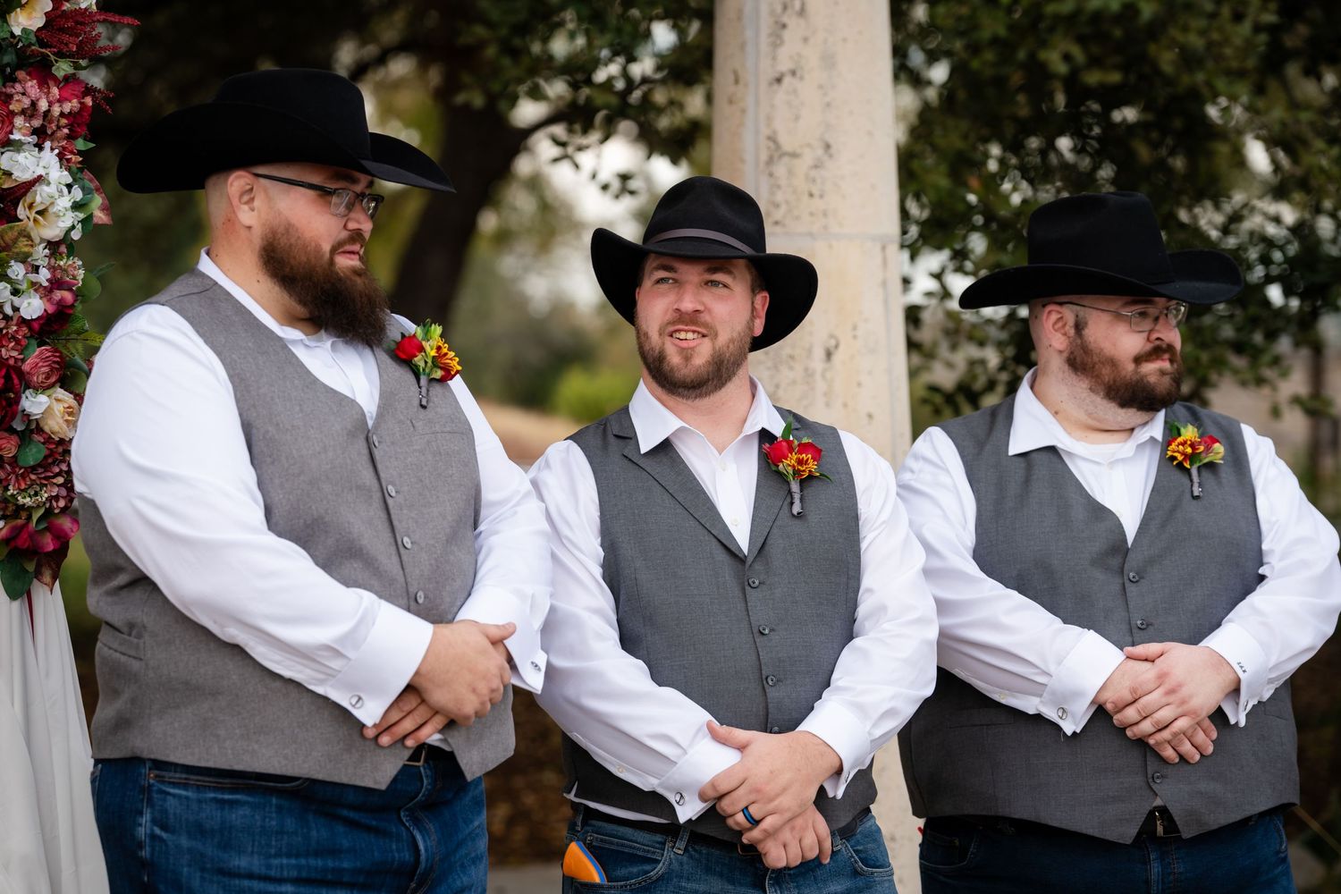 Three groomsmen in matching western attire with black cowboy hats, vests, and white shirts pose together at a wedding.