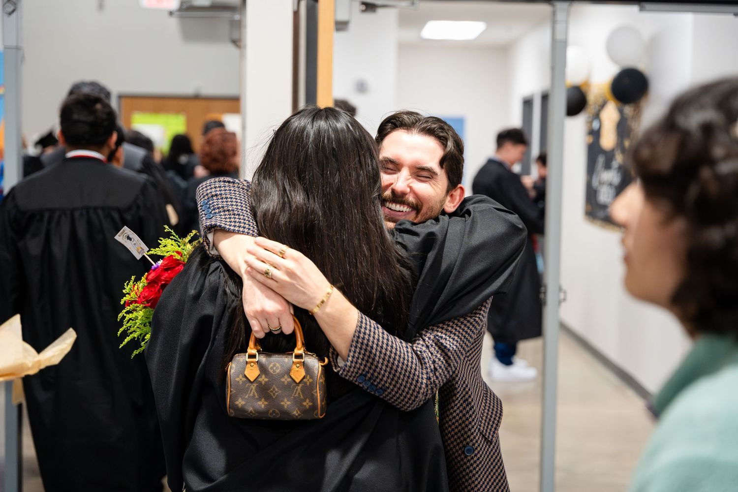 Emotional graduation celebration with hugs and flowers in school hallway.