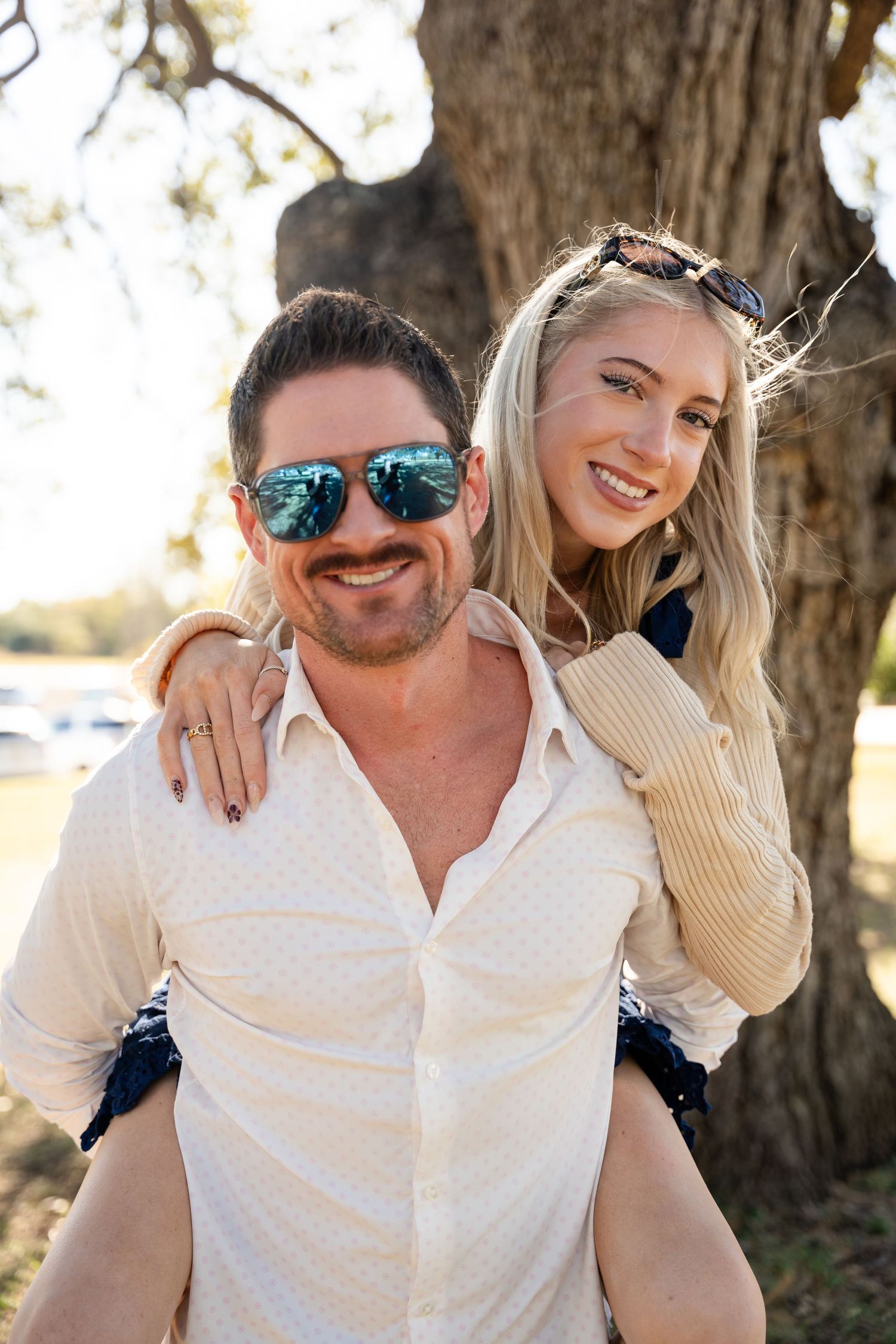 A couple shares a playful moment outdoors near a large tree.