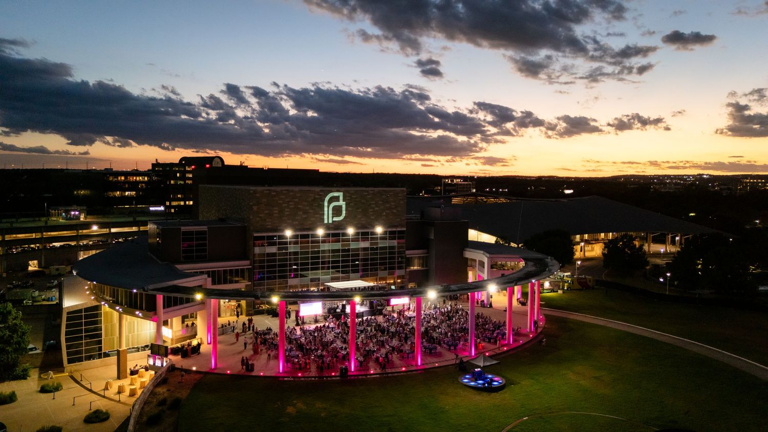 Dramatic sunset view of outdoor event space illuminated with pink lighting and modern building backdrop.