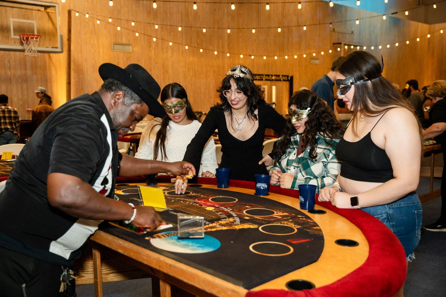 Casino night event with people gathered around a curved gaming table under string lights.