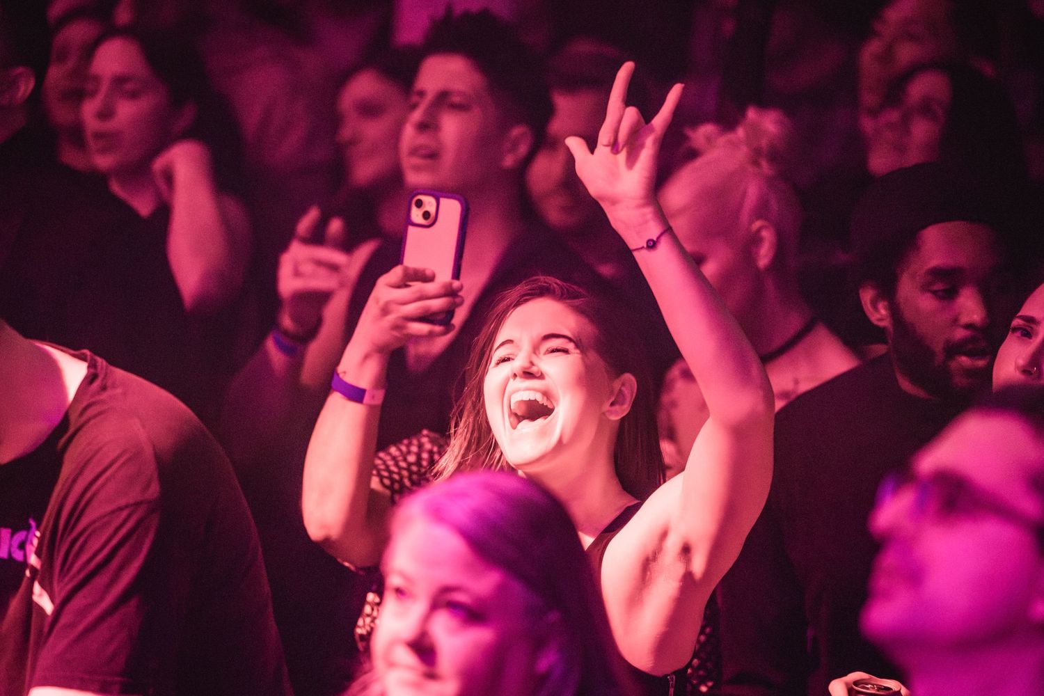 Enthusiastic crowd enjoying live music under pink and purple concert lighting.