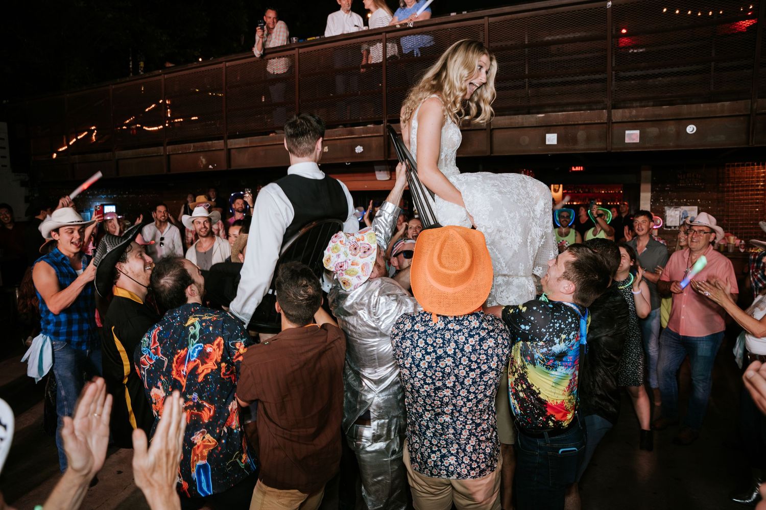 A bride gets lifted up by guests during an energetic wedding reception dance party.