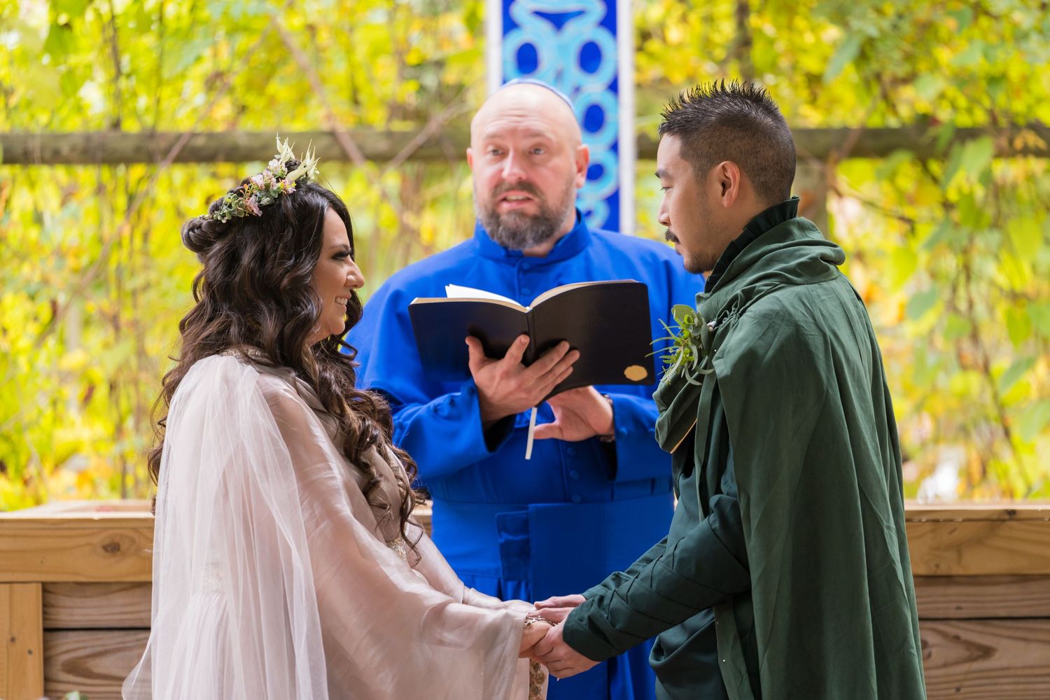 An outdoor wedding ceremony under autumn foliage with three people at a wooden altar.