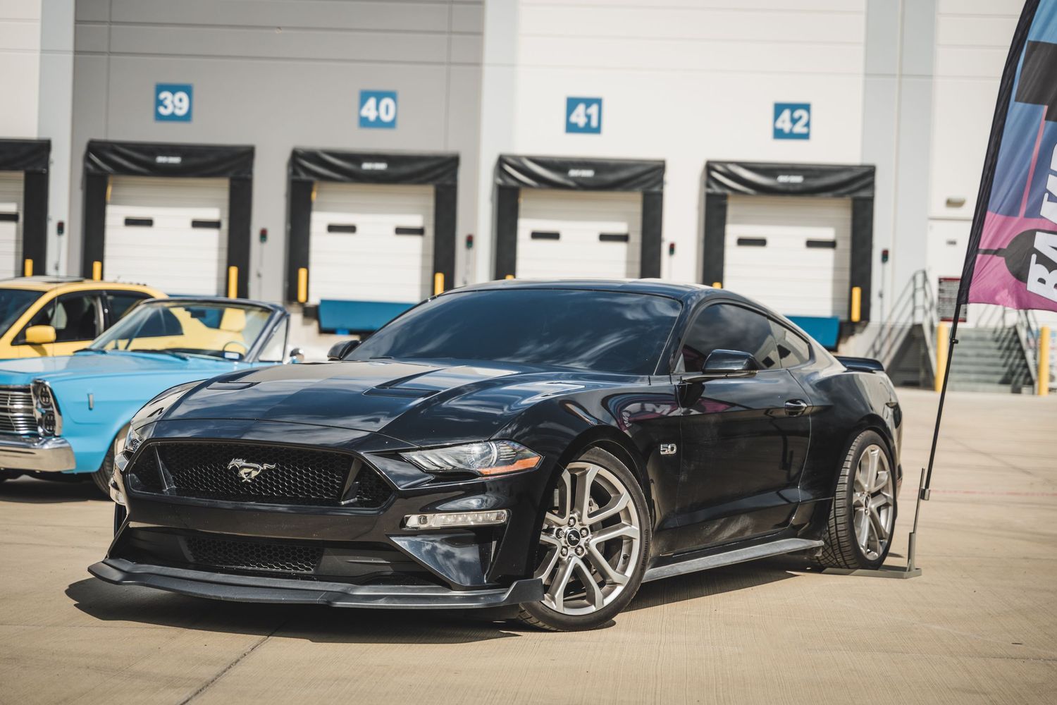 Black Ford Mustang GT with custom wheels and body modifications at loading area.