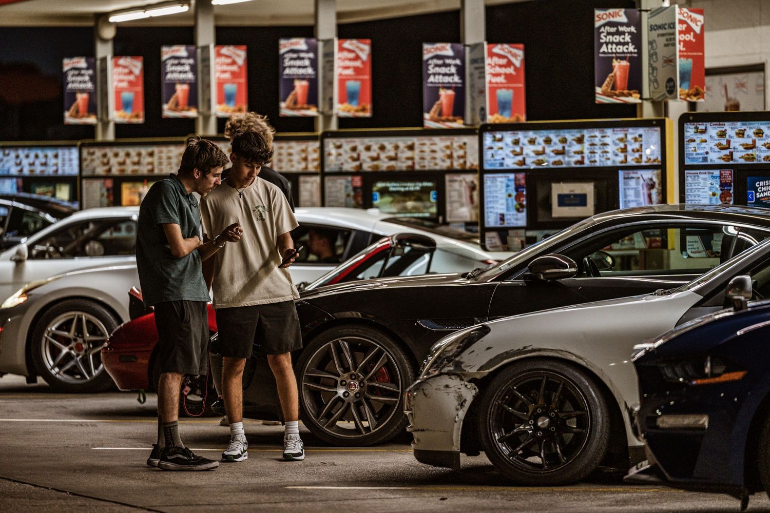 Car enthusiasts gather around luxury sports cars at a nighttime auto meet.