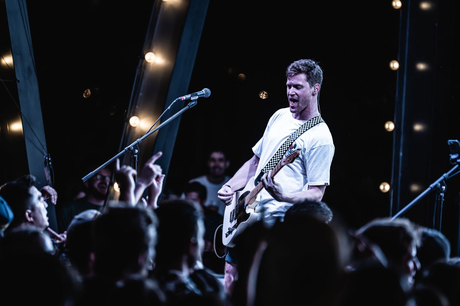 Guitarist performs on elevated stage with string lights above crowd.