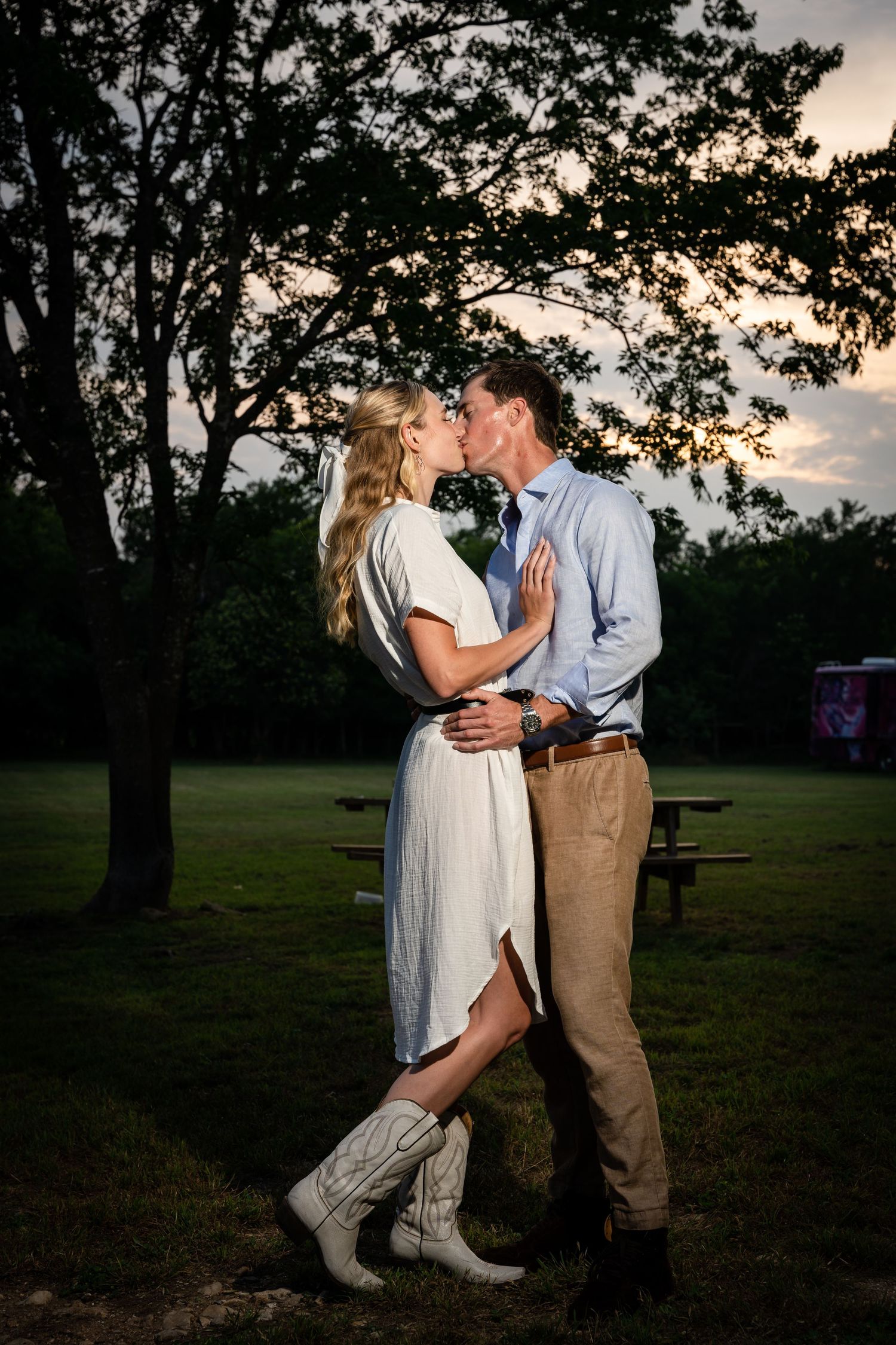 Couple in coordinating outfits embrace in a park during golden hour.