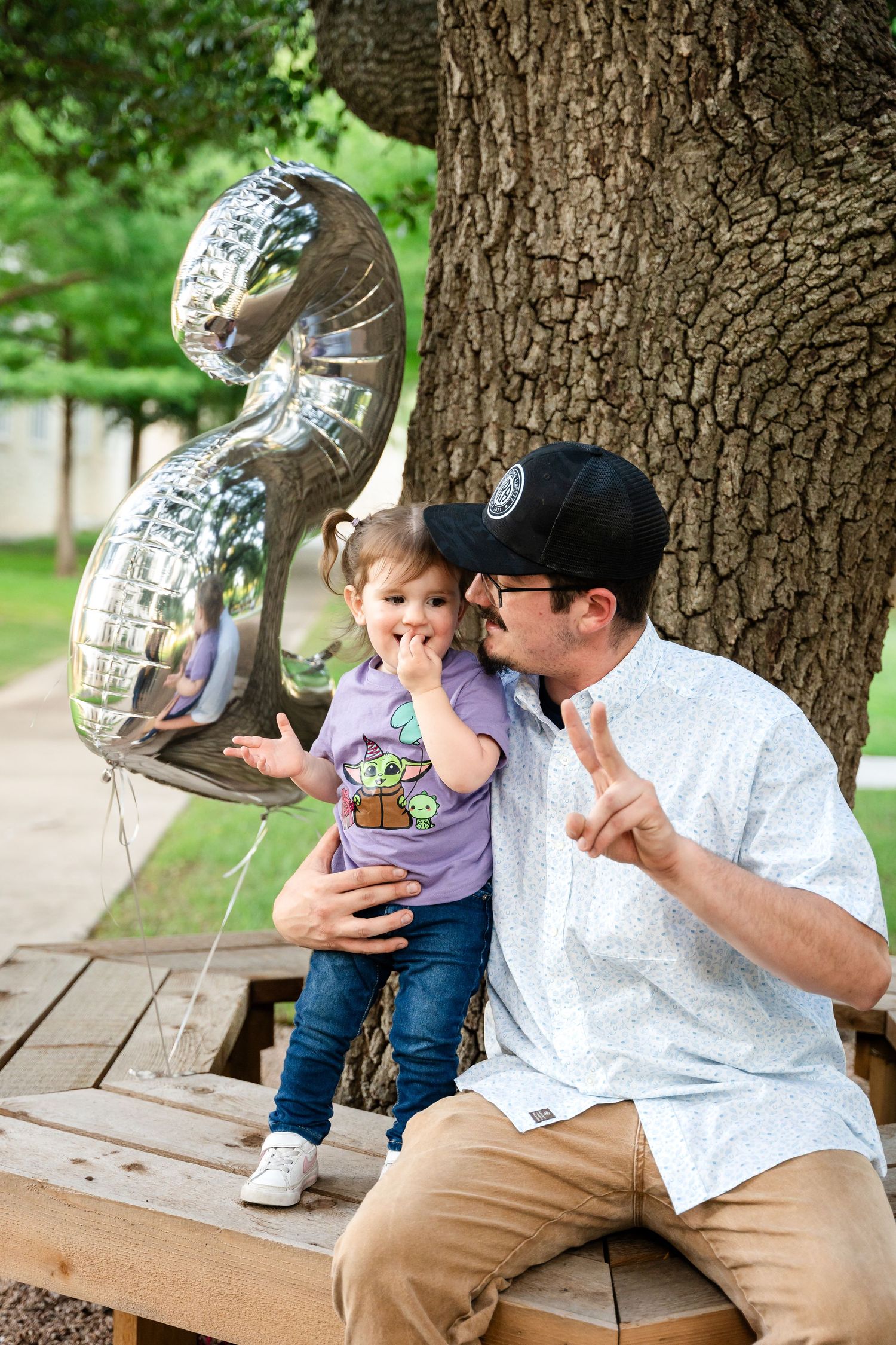 A playful moment with silver number balloons by a large tree trunk.
