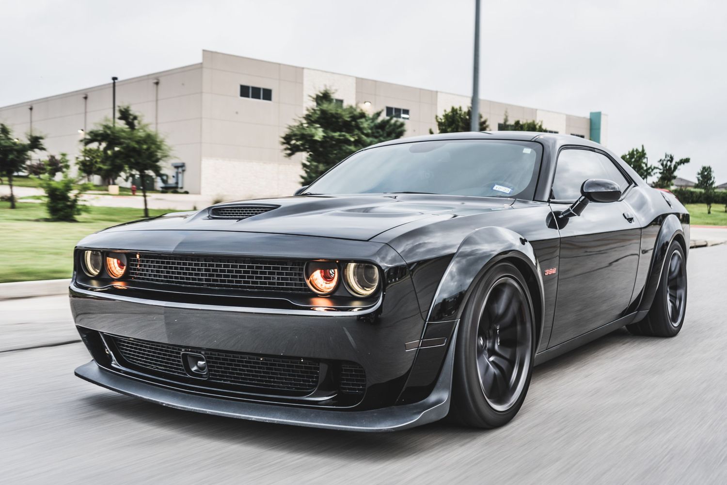 Modified Dodge Challenger Hellcat with black wheels and custom bodywork cruising on urban road.