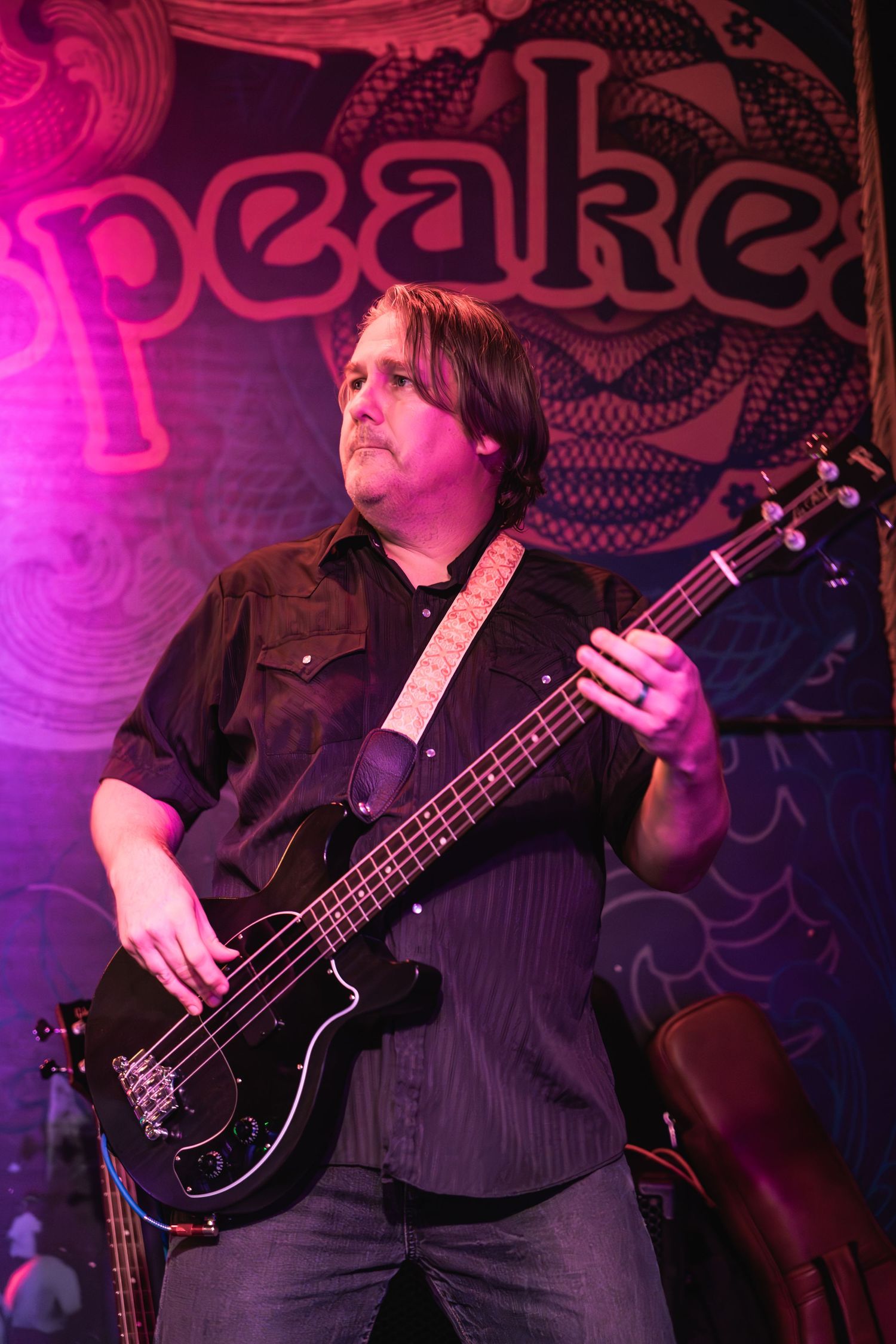Bass player performs under pink stage lights with band logo visible in background.
