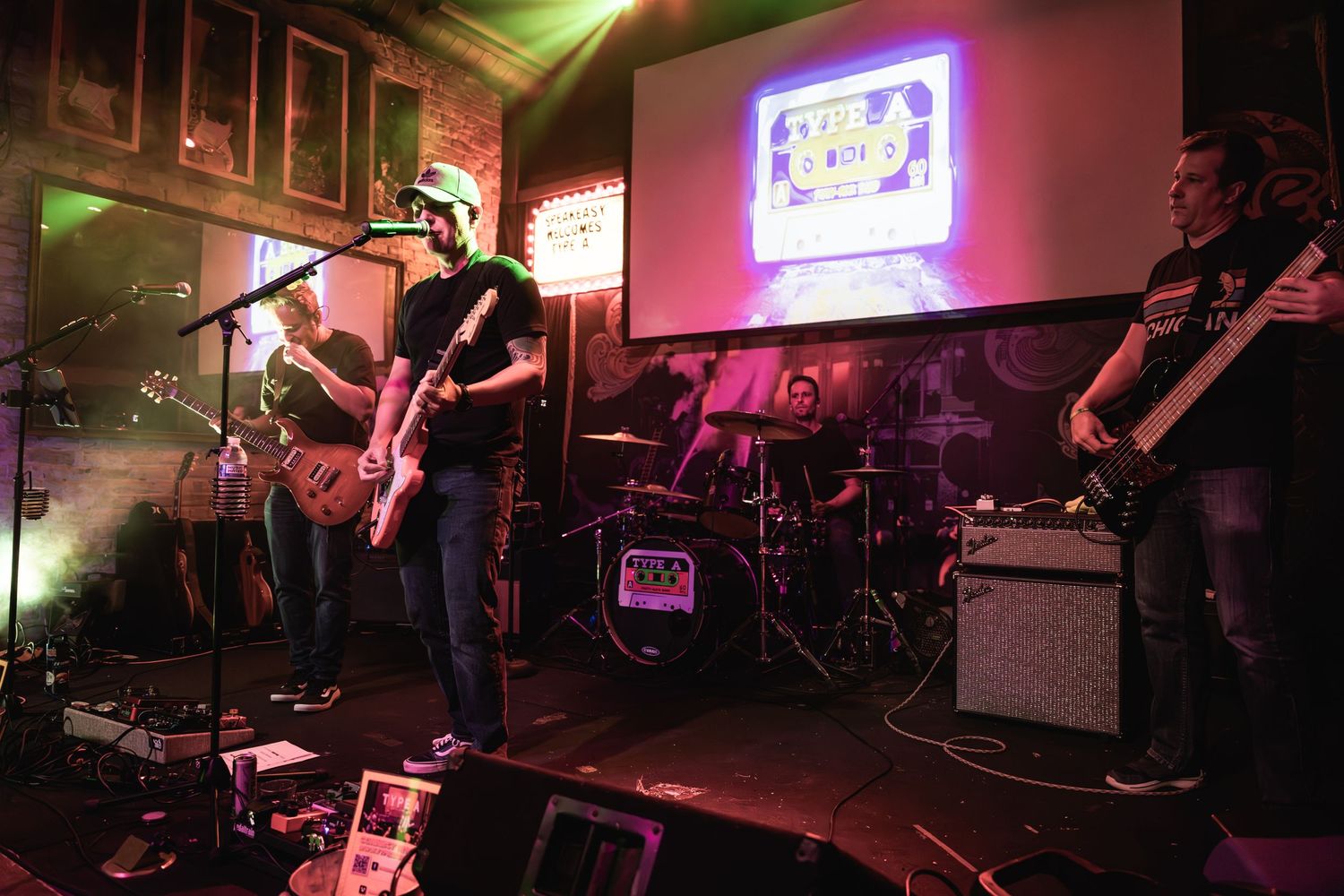 A band performs on stage with colorful lighting and projection screens in the background.