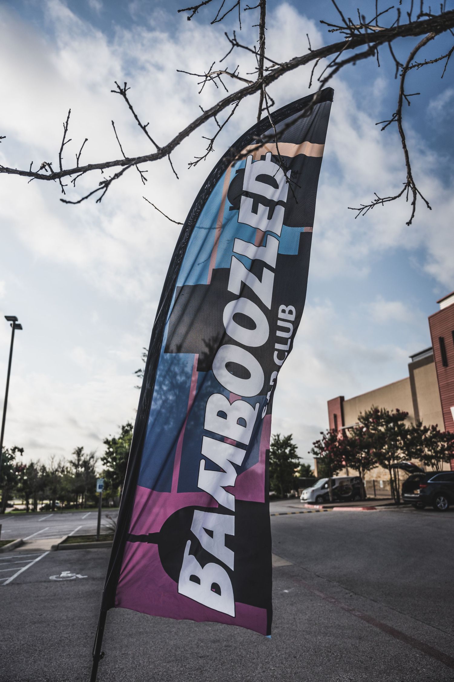 Vertical banner flag displaying Bamboozler club branding against a cloudy sky.