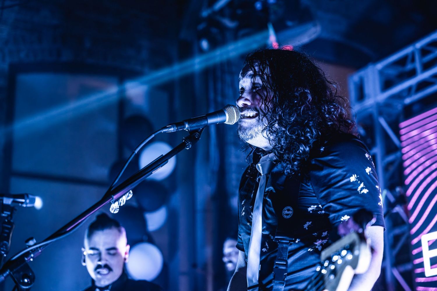 Musician singing into microphone on stage with dramatic blue lighting.