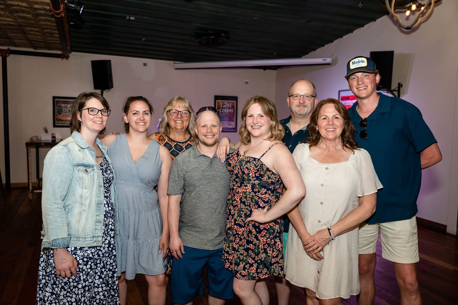 A group of friends pose together at a social gathering inside a dimly lit venue.