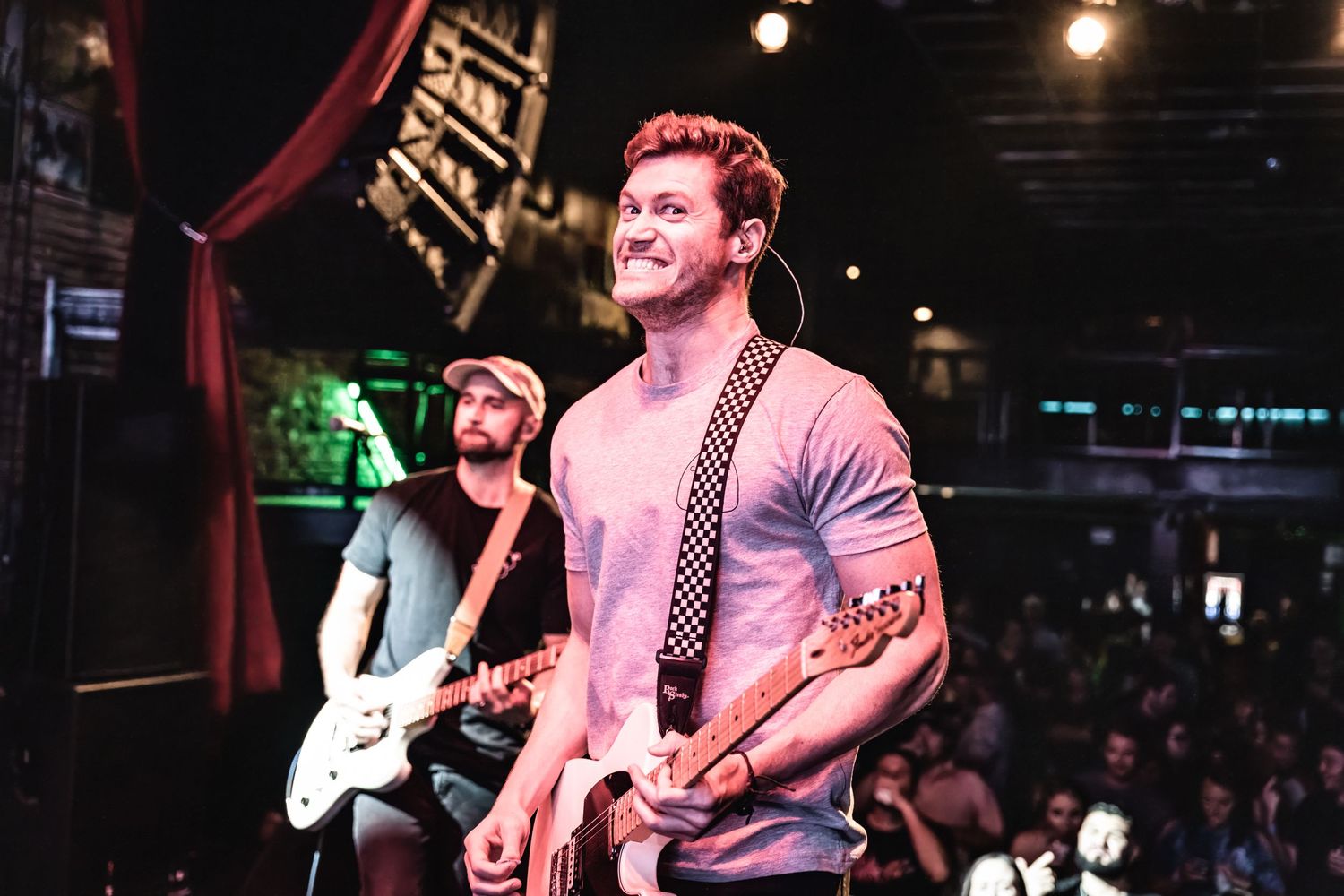 Musicians perform energetically on stage under pink and red lighting at intimate venue concert.