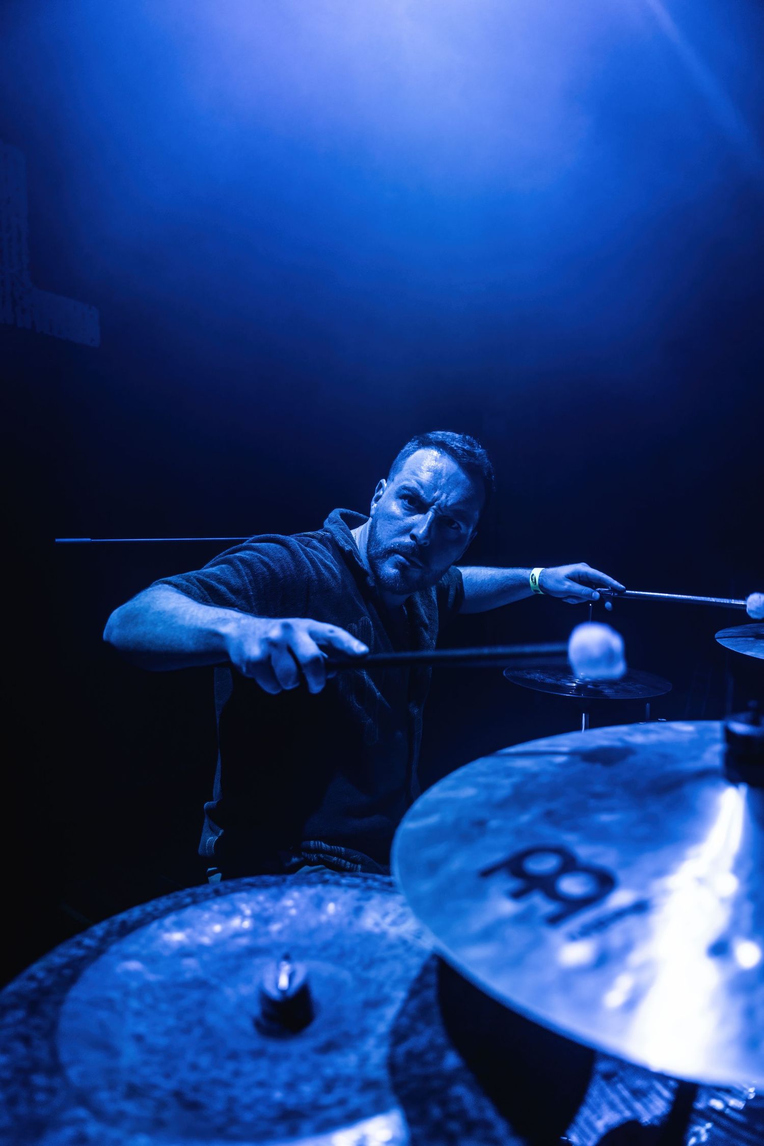 Drummer intensely plays cymbals bathed in blue stage lighting during performance.
