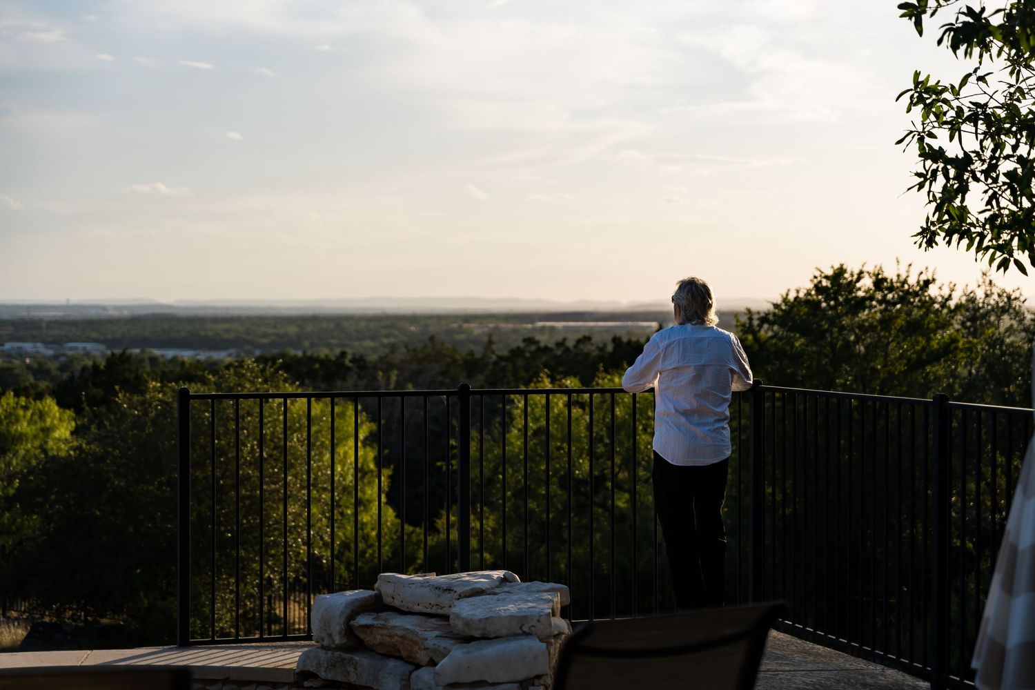 Person looking out over scenic vista from outdoor deck at sunset.