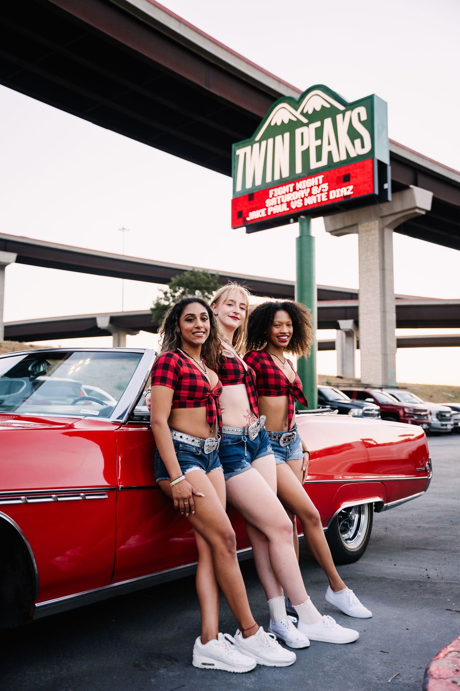Friends posing by classic red convertible under Twin Peaks restaurant sign.