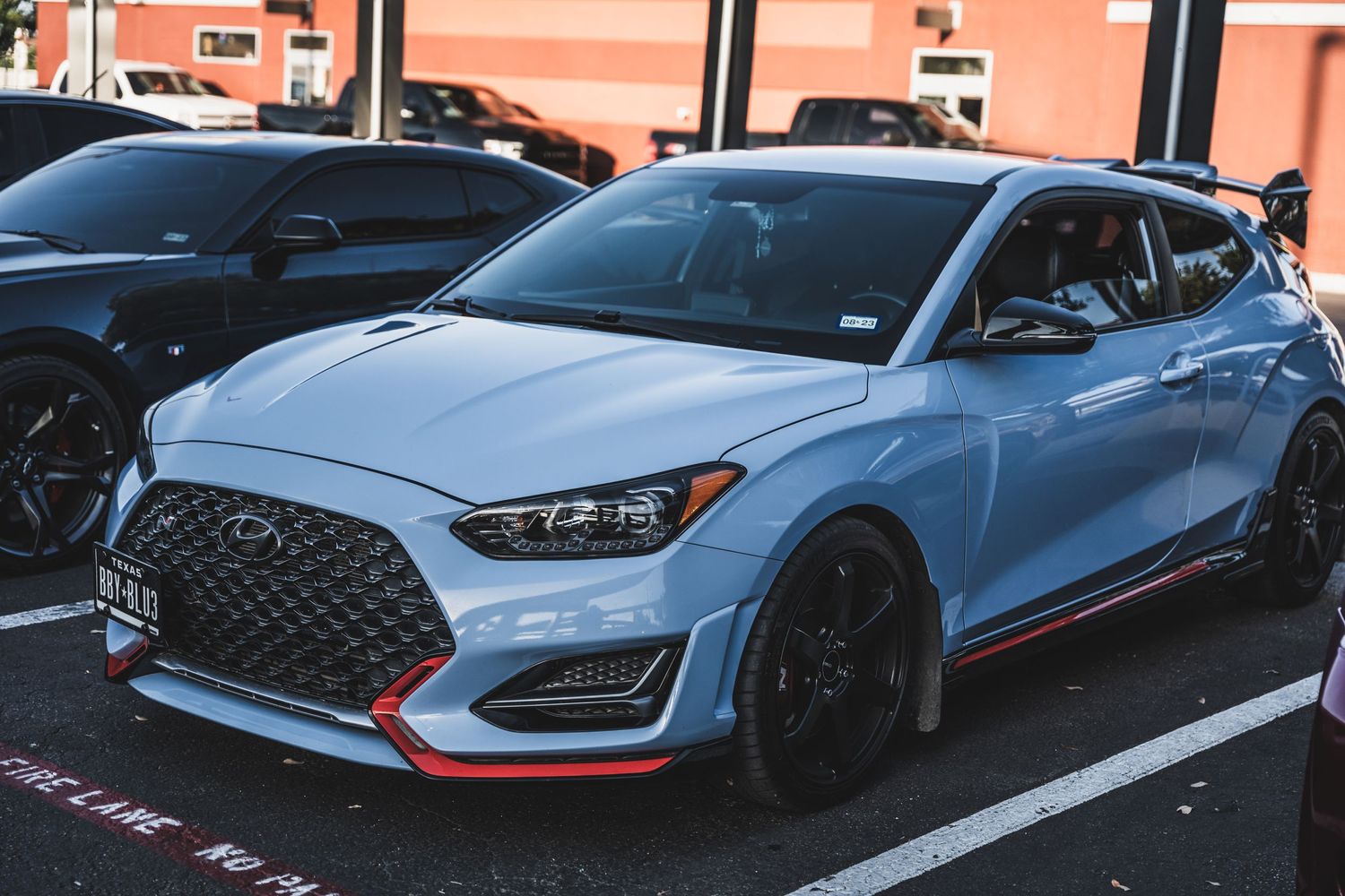 Light blue Hyundai Veloster N with black wheels and red accents parked in a lot.