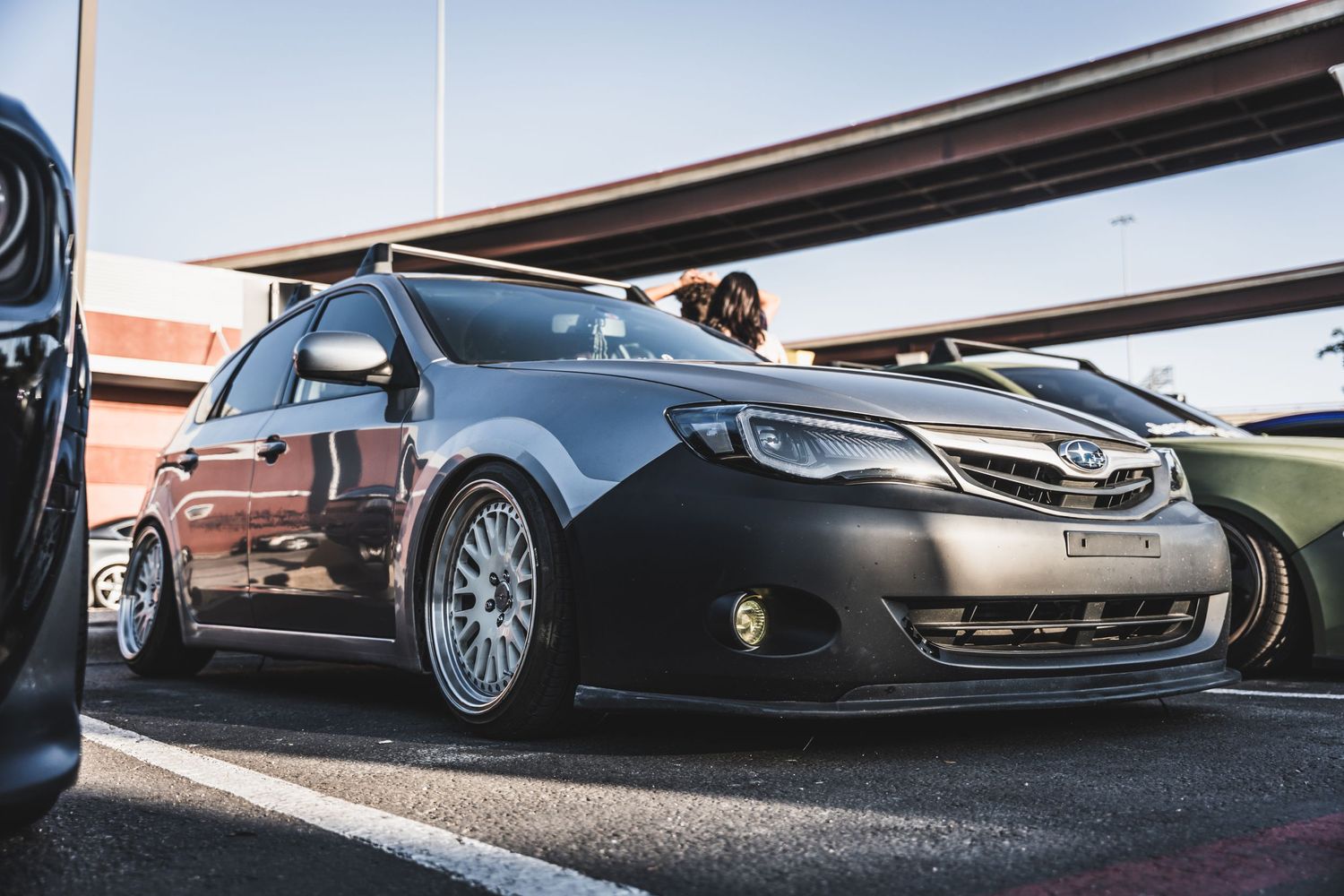 Lowered Subaru WRX with custom BBS wheels parked under an industrial structure.