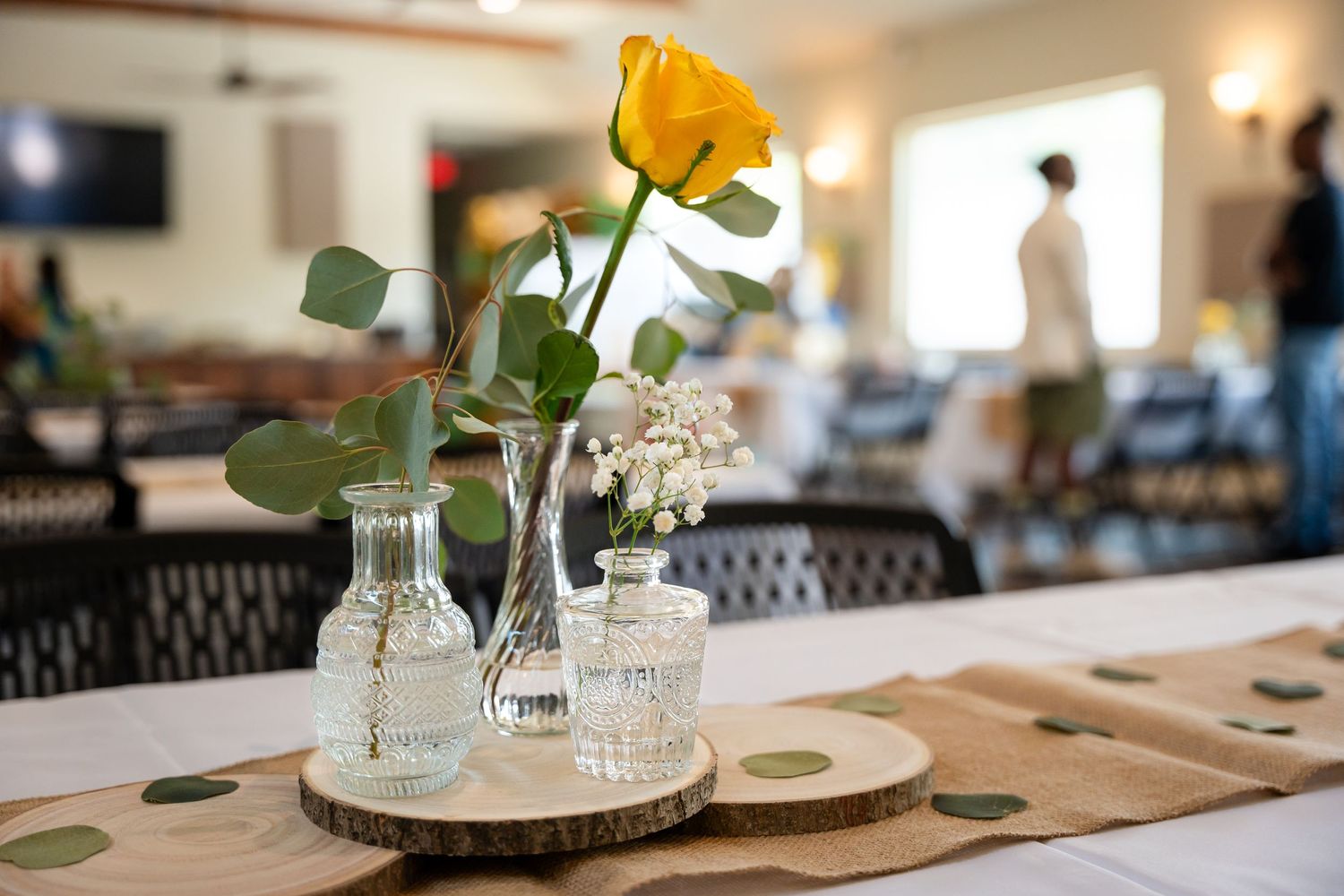 Yellow rose centerpiece in vintage glass bottles on rustic wooden table.
