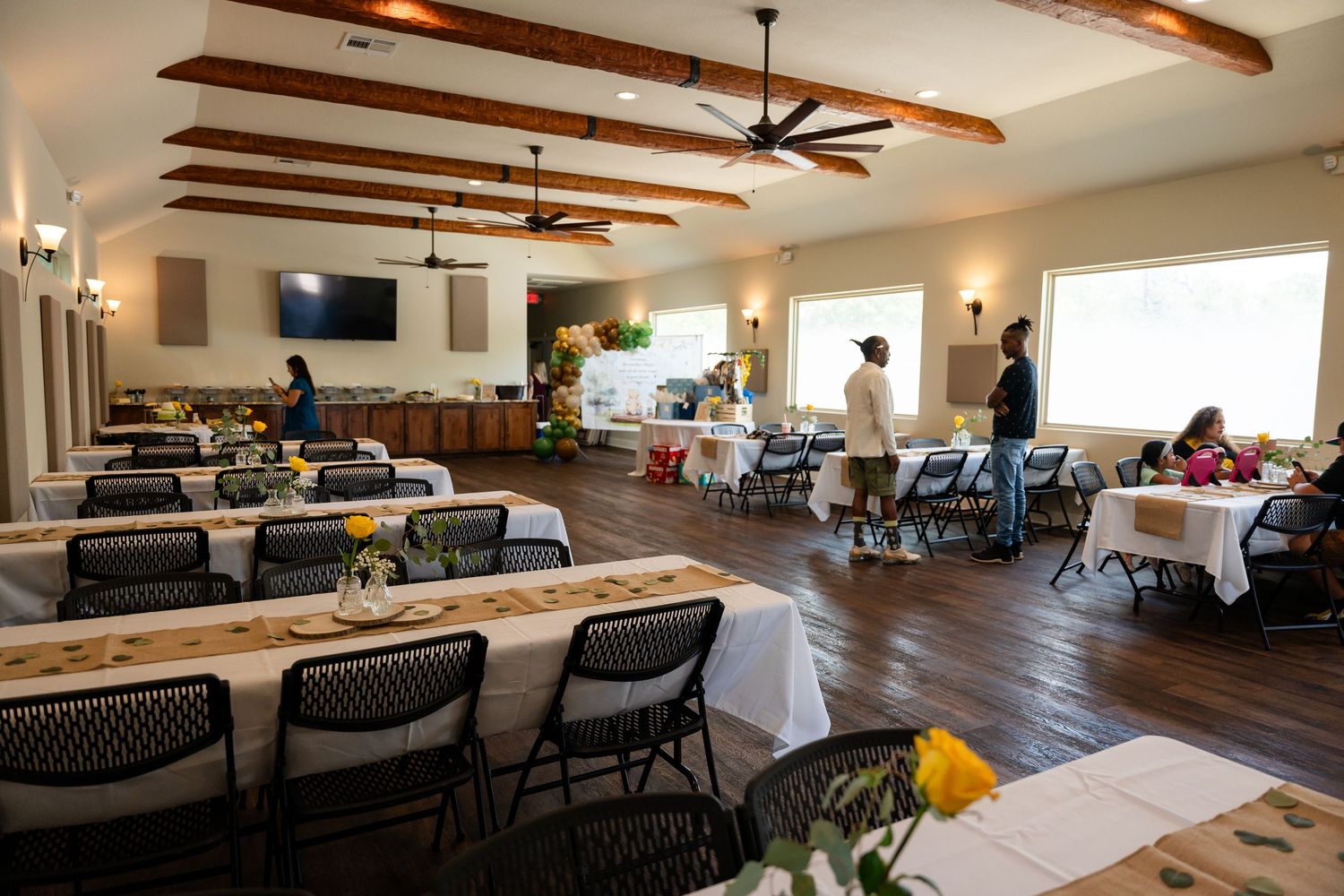 Large event space with wooden floors and exposed beams featuring tables and chairs set up for a gathering.