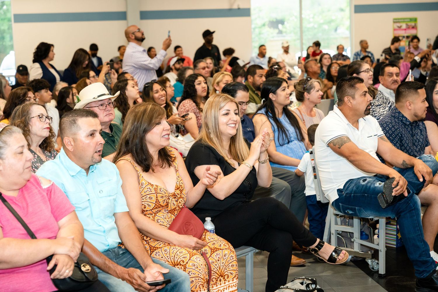 An engaged audience watches intently during an indoor event in a bright room with blue accent walls.
