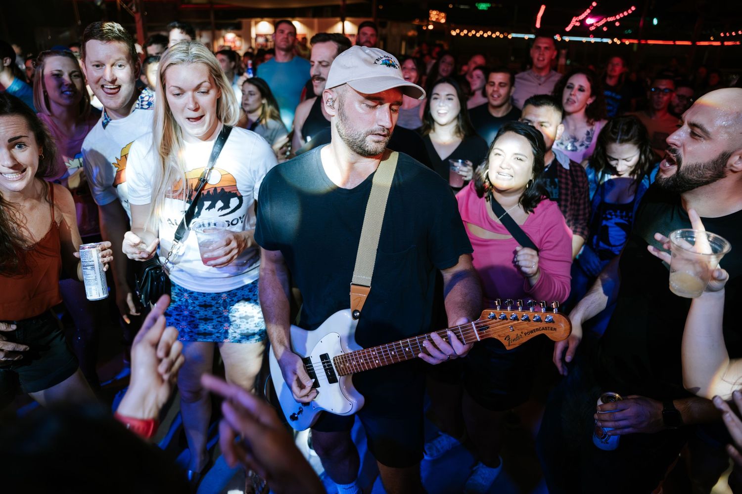 Concert performer with guitar entertains animated crowd in dimly lit music venue.