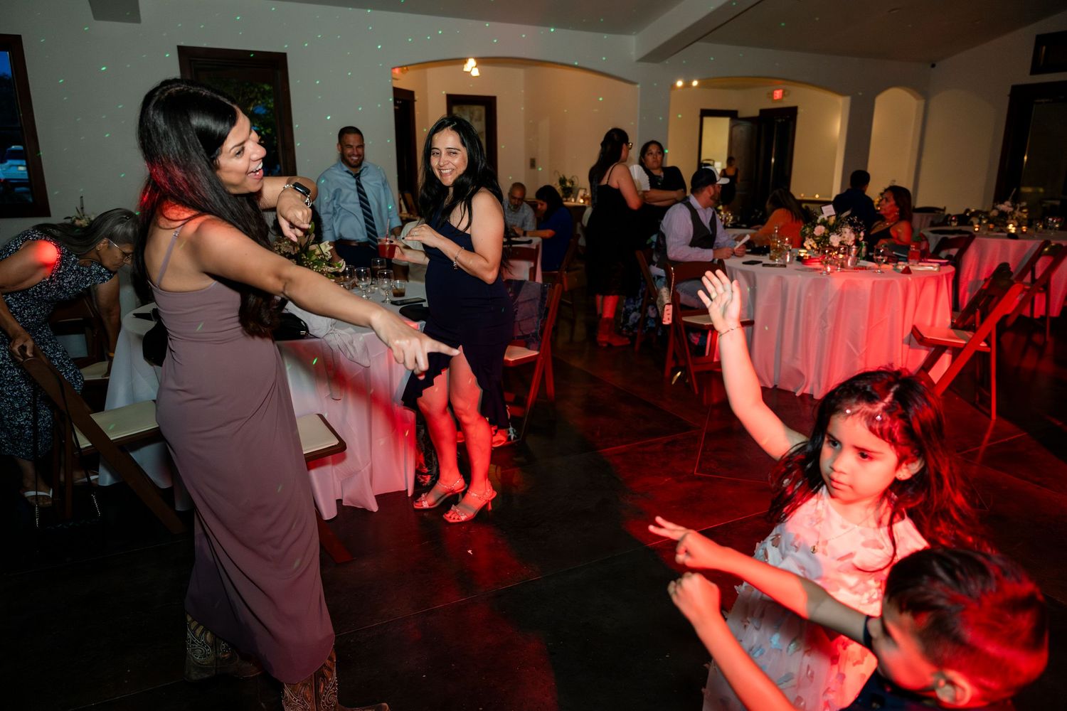 People dancing at a reception under red lighting in a dimly lit banquet hall.
