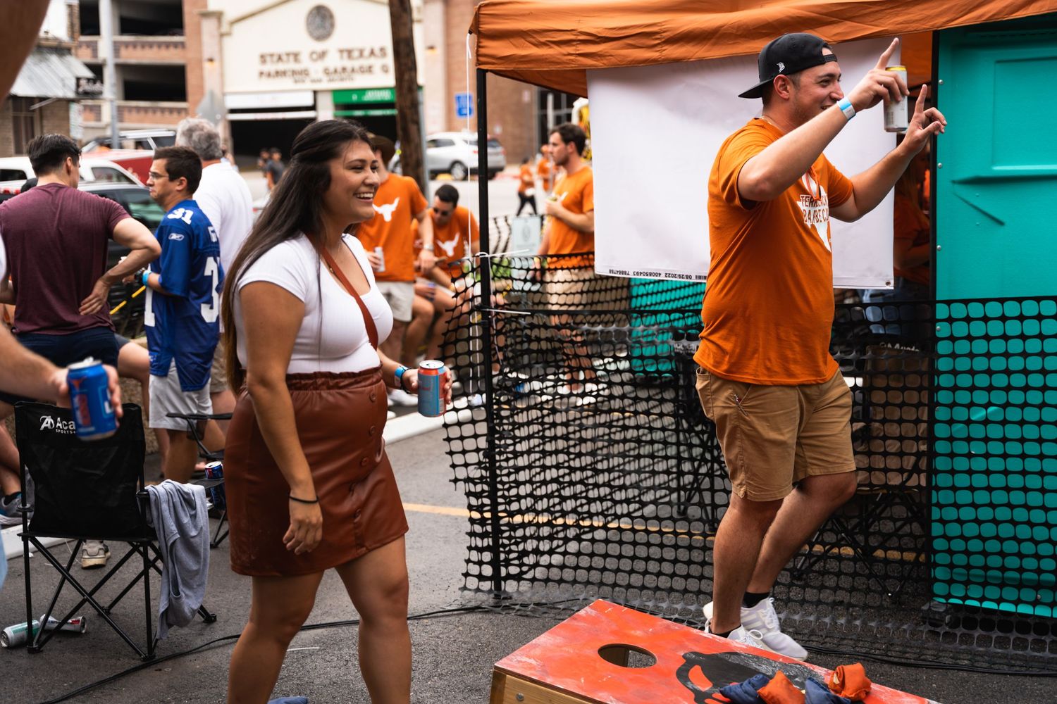 People enjoying outdoor festival activities with cornhole game setup.