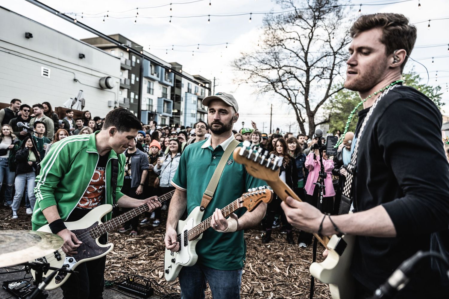 Band performing live music with guitarists in green and black outfits at outdoor venue.