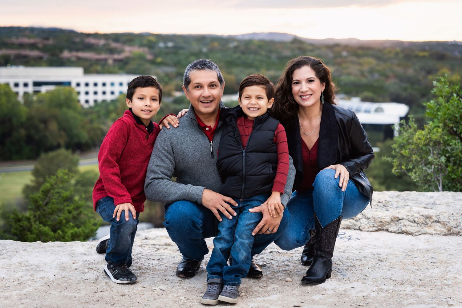 Family portrait of four people dressed casually sitting together on a stone ledge with scenic landscape behind them.