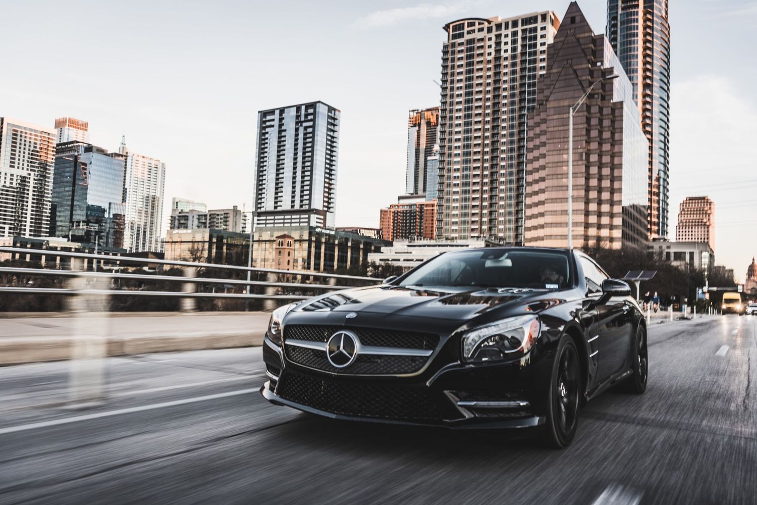 Black Mercedes-Benz cruising through downtown Austin with iconic skyline in background.