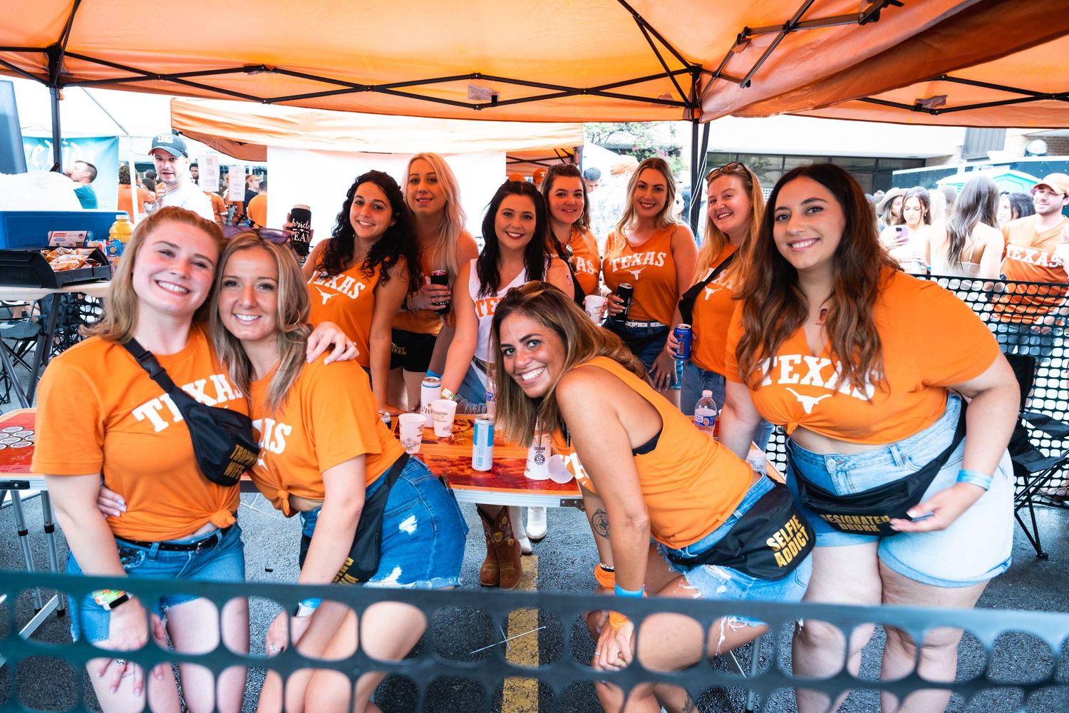 A group wearing orange shirts enjoys food and drinks at an outdoor tailgate party.