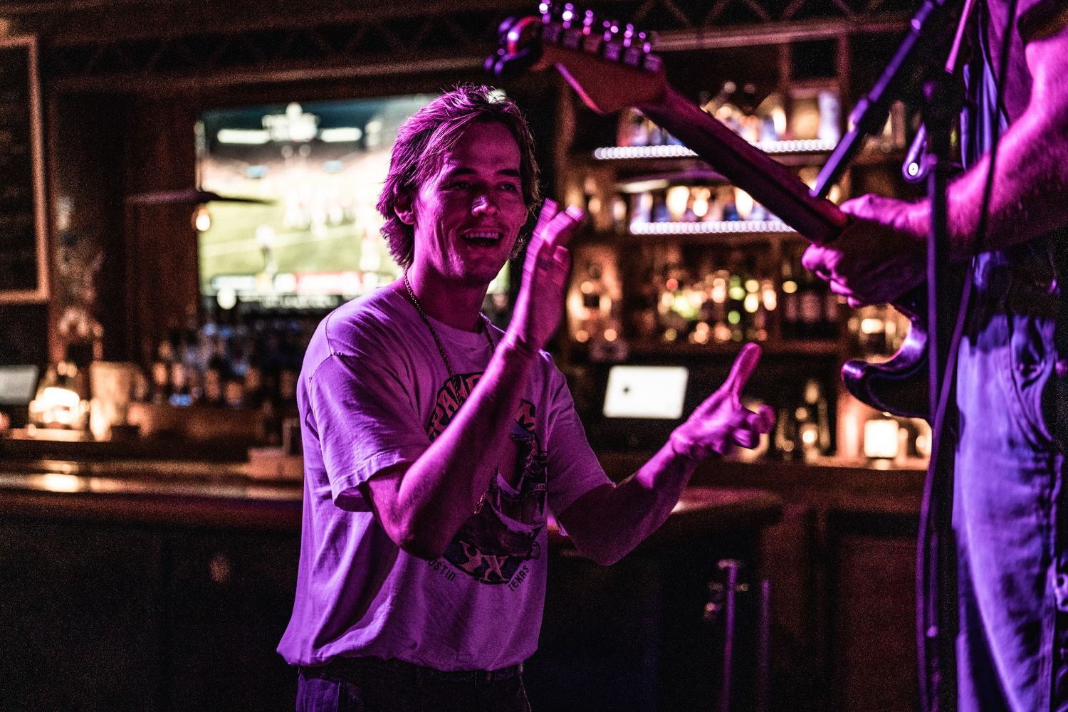 Performers play instruments on dimly lit bar stage with purple ambient lighting.