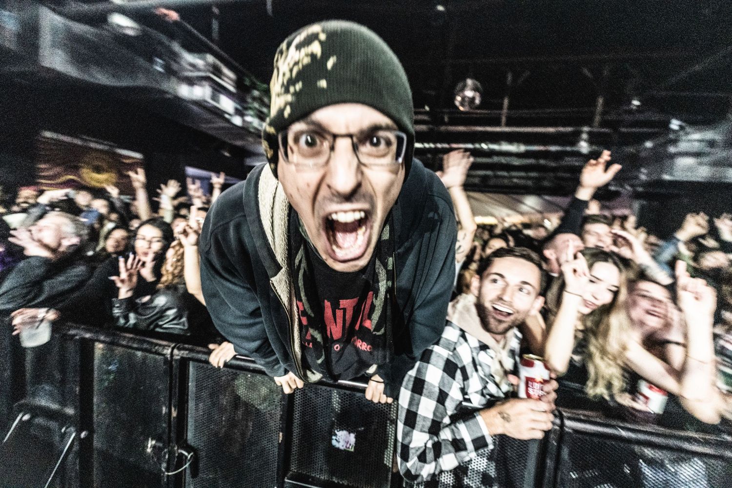 Energetic performer leaning into crowd during concert with enthusiastic fans.