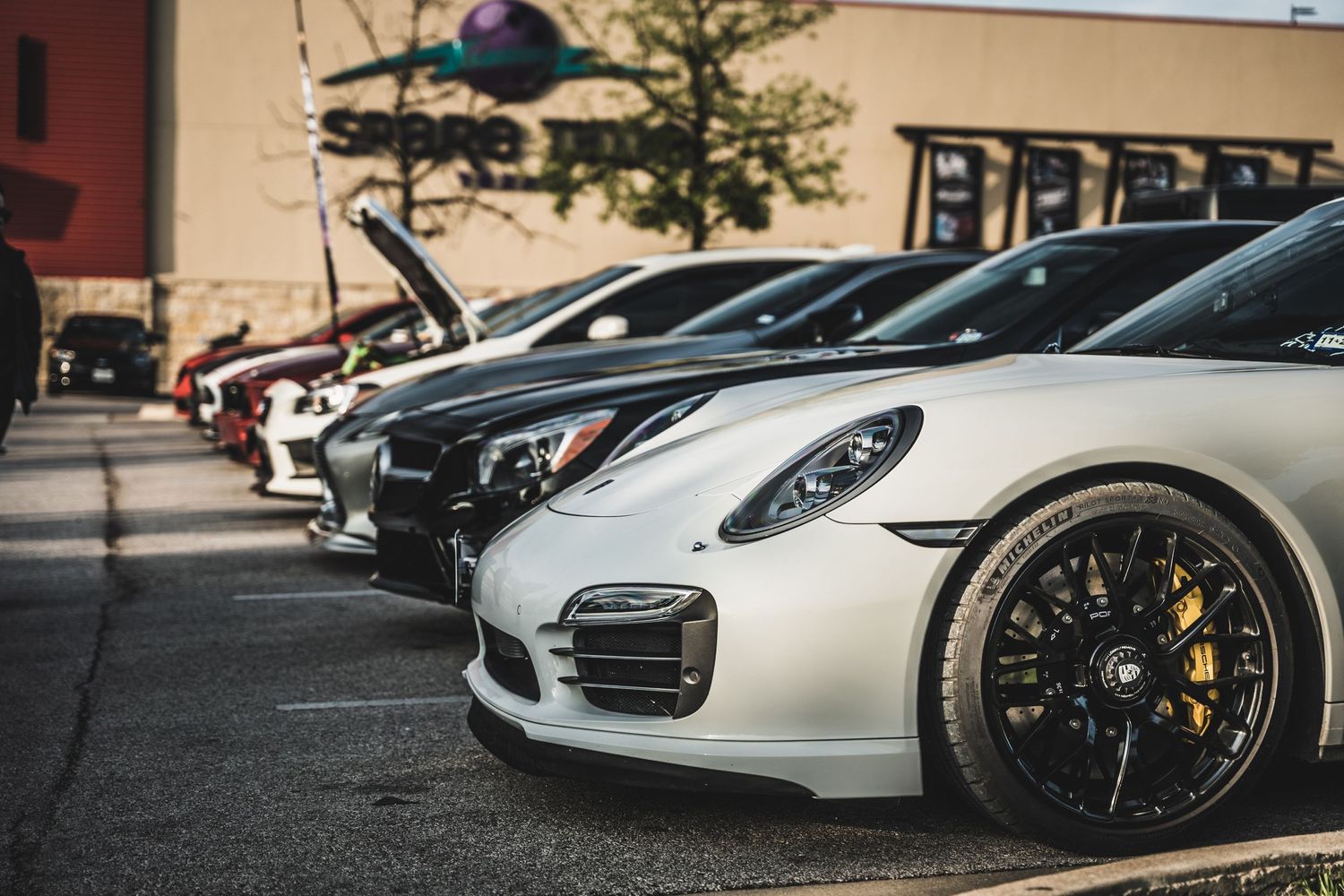 Row of high-end Porsche sports cars showcasing sleek designs and custom wheels in a parking lot.