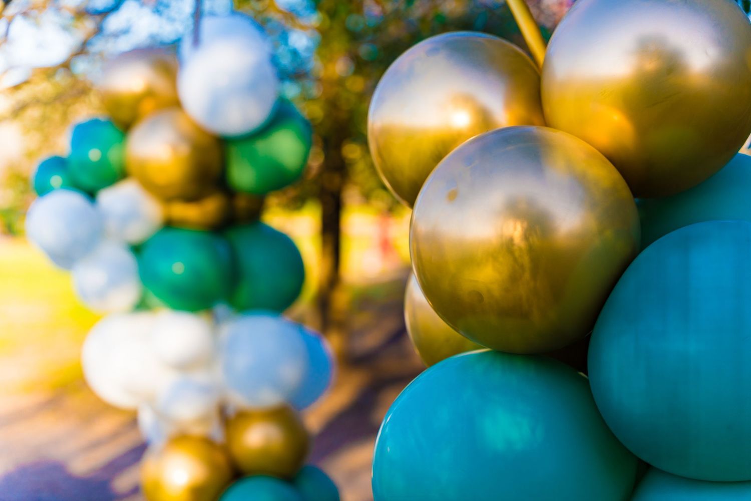 Detailed view of metallic gold and turquoise balloons in sunlit outdoor setting.