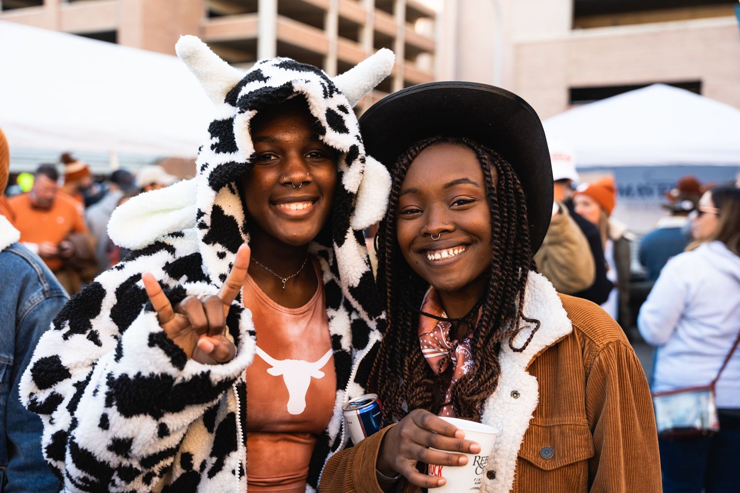 Two friends in western and animal print outfits sharing laughs at outdoor festival.