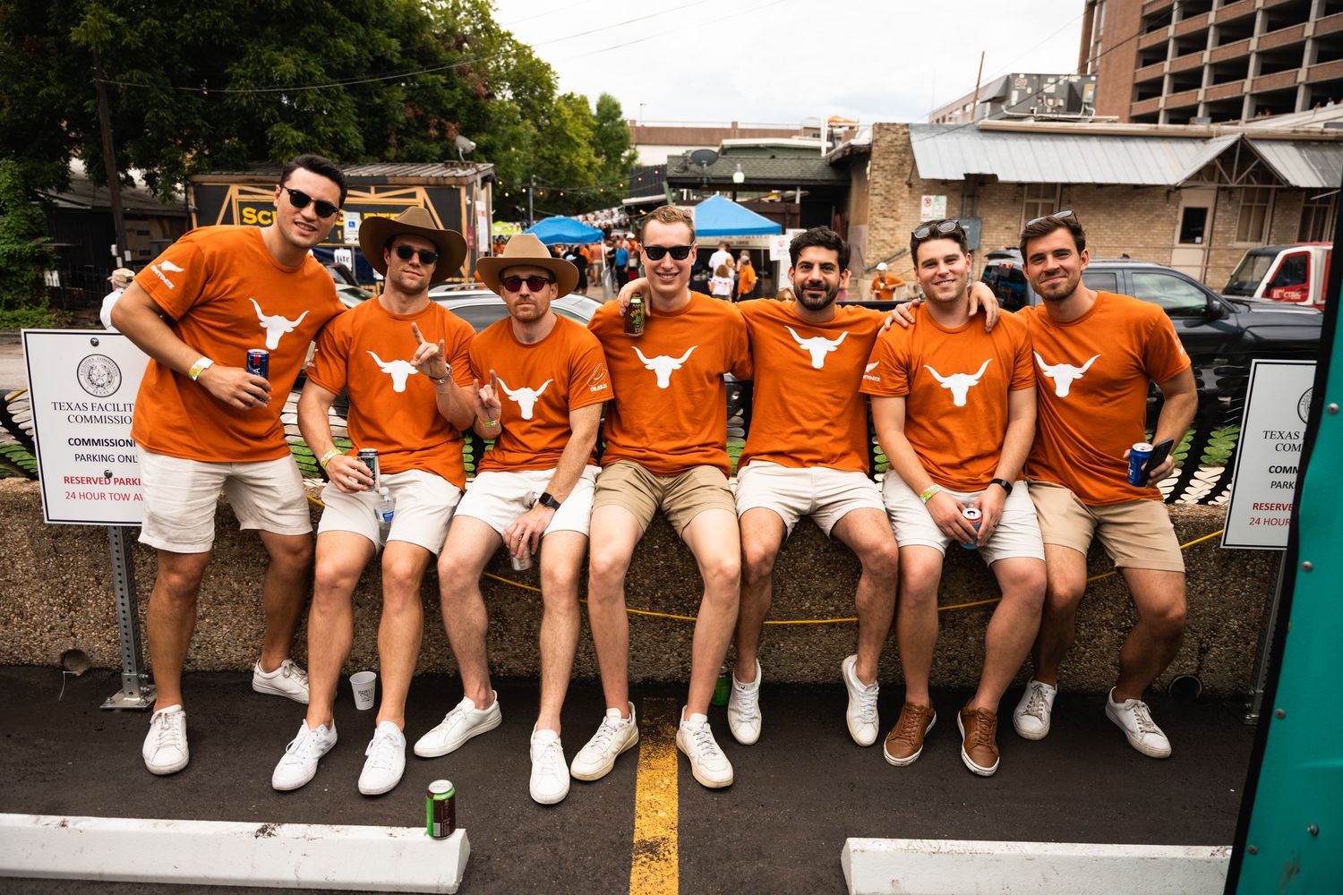Group wearing matching burnt orange shirts and khaki shorts posing together at a tailgate event.